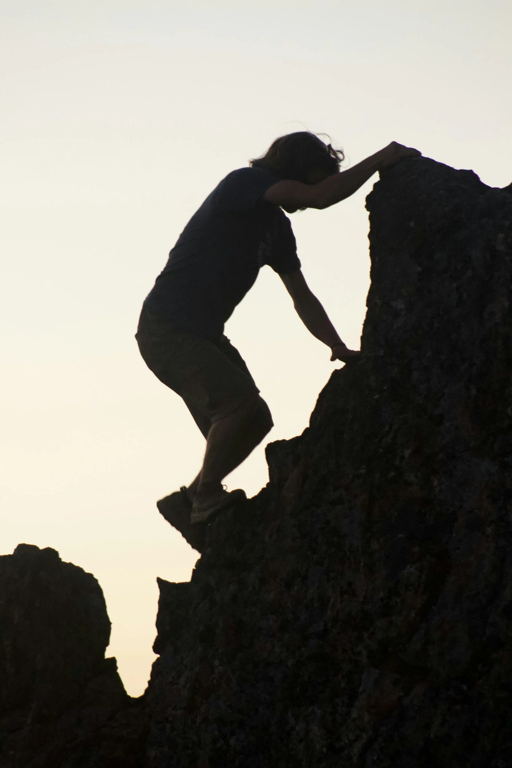 Person climbing rocky terrain during sunset or sunrise.