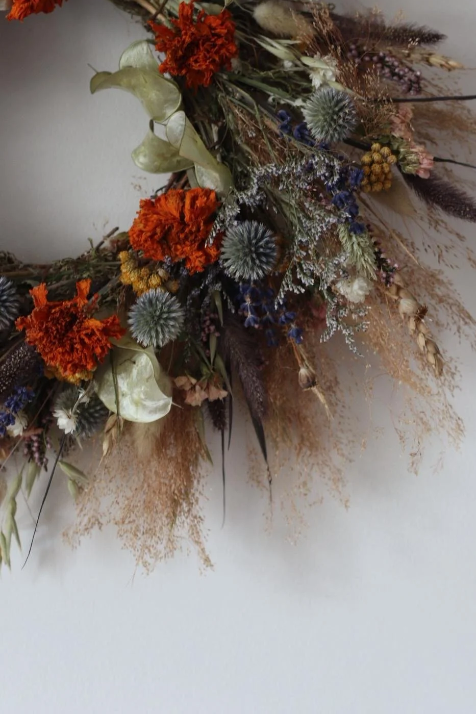 A close-up of a dried floral arrangement featuring orange, white, purple, and beige flowers, along with various dried grasses and foliage.