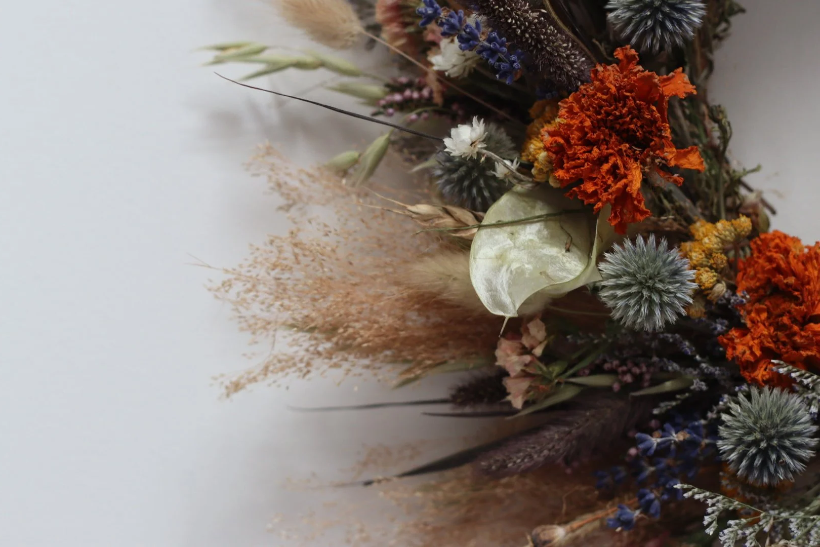 A dried flower arrangement with orange, white, purple, and gray flowers and foliage on a neutral background.