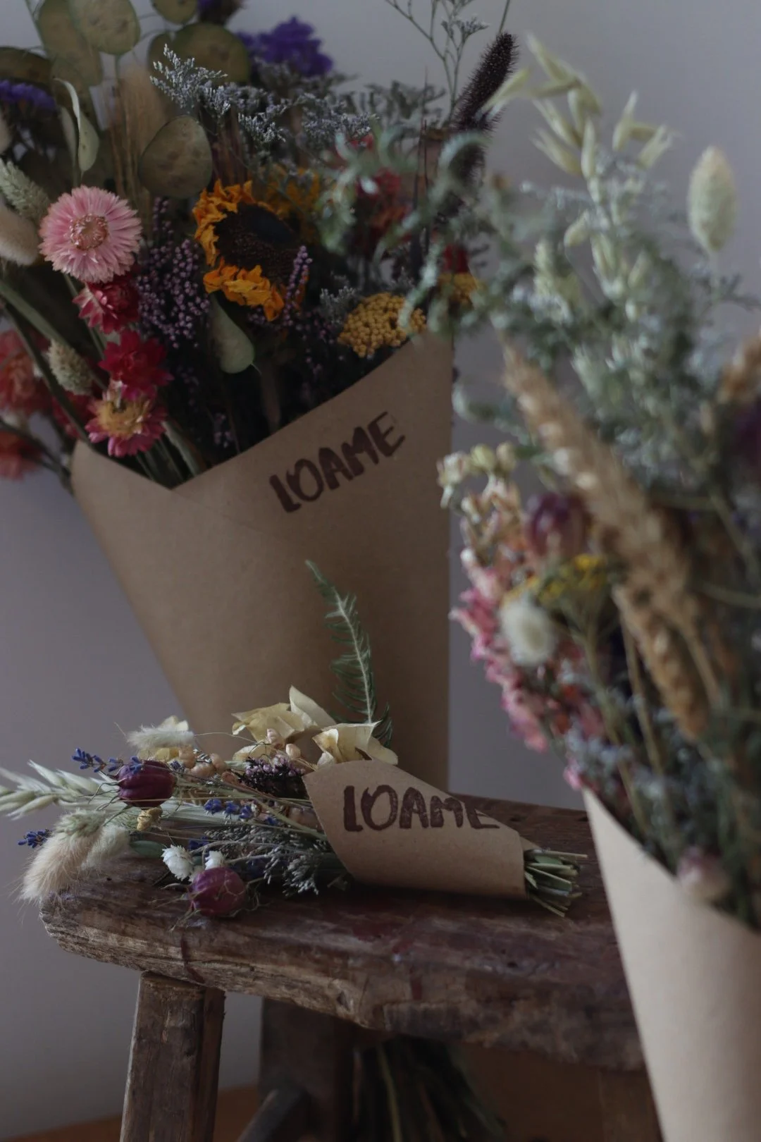Dried flower bouquets wrapped in brown paper labeled "LOAVE" resting on a rustic wooden surface.