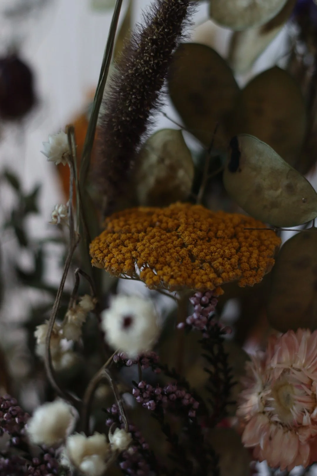 Close-up of a dried flower arrangement with yellow, pink, and white flowers, and eucalyptus leaves in a muted color palette.