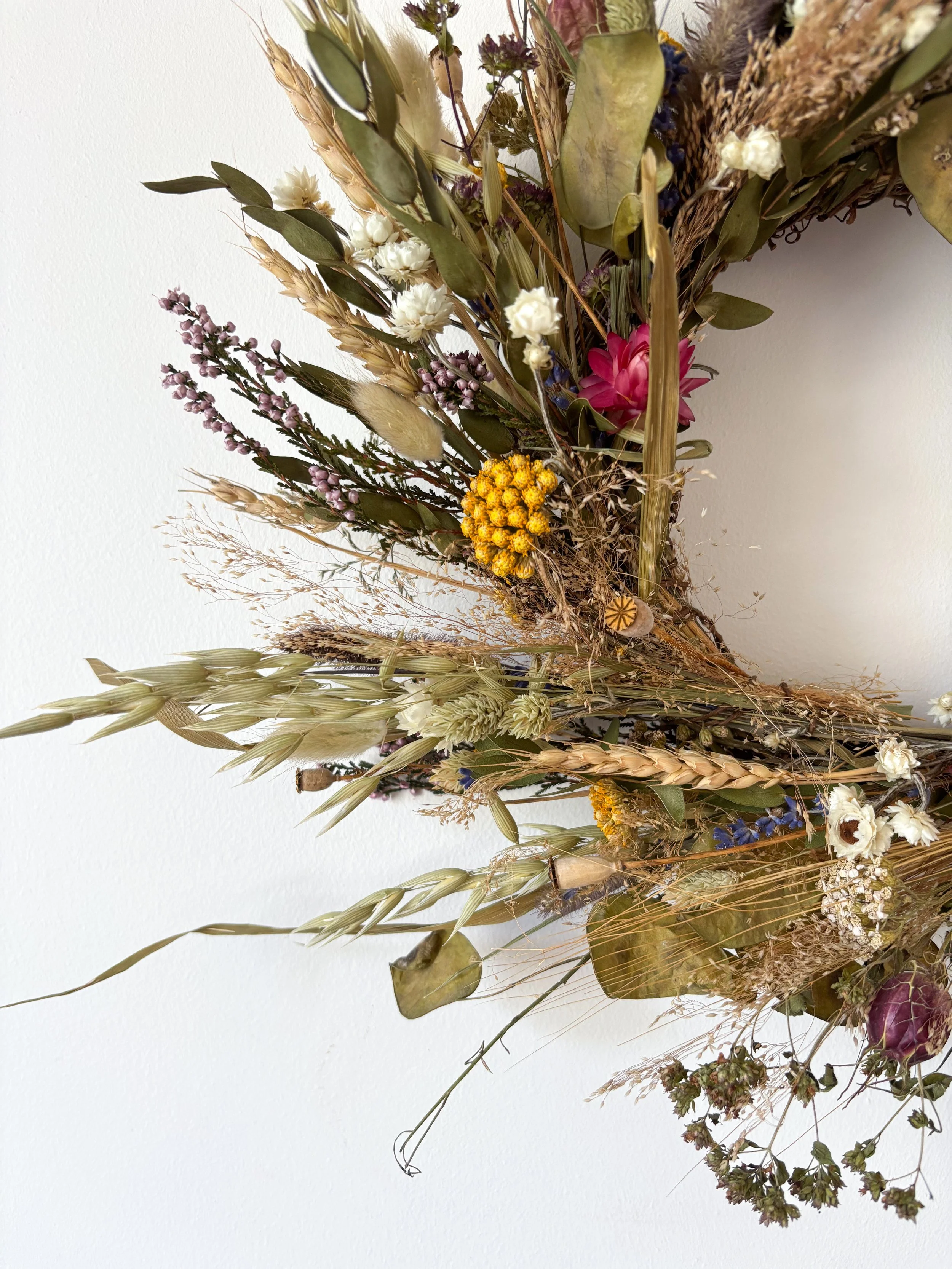A dried floral arrangement with various flowers and grasses against a plain white background.