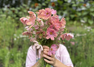 A person holding a bouquet of pink flowers in front of their face in a garden