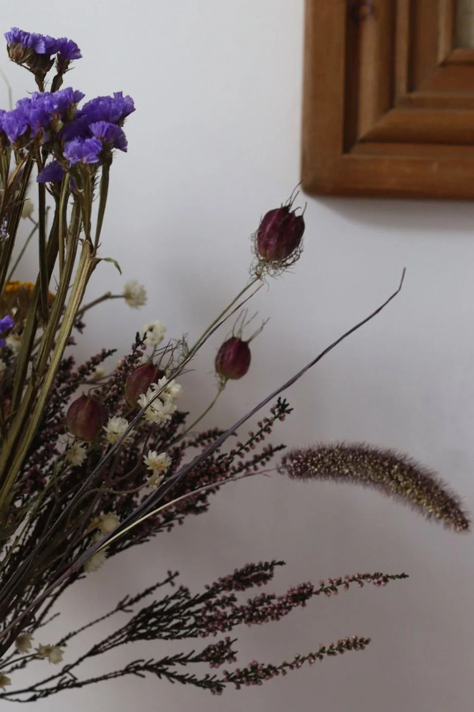 Dry bouquet of wildflowers and ornamental grasses on a white background, with a wooden frame visible in the top corner.