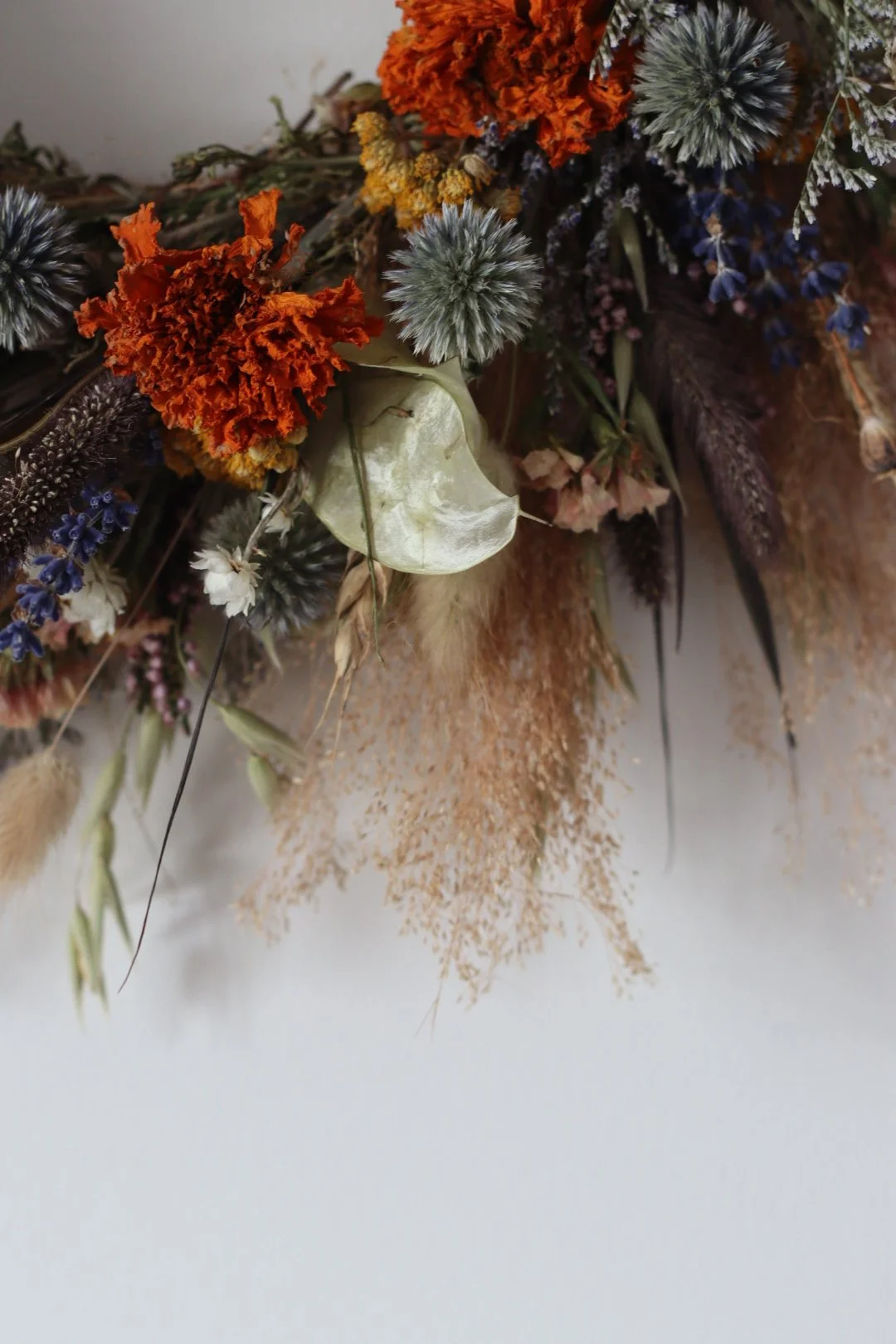 Close-up of a dried flower arrangement featuring orange, gray, purple, and beige flowers and foliage.