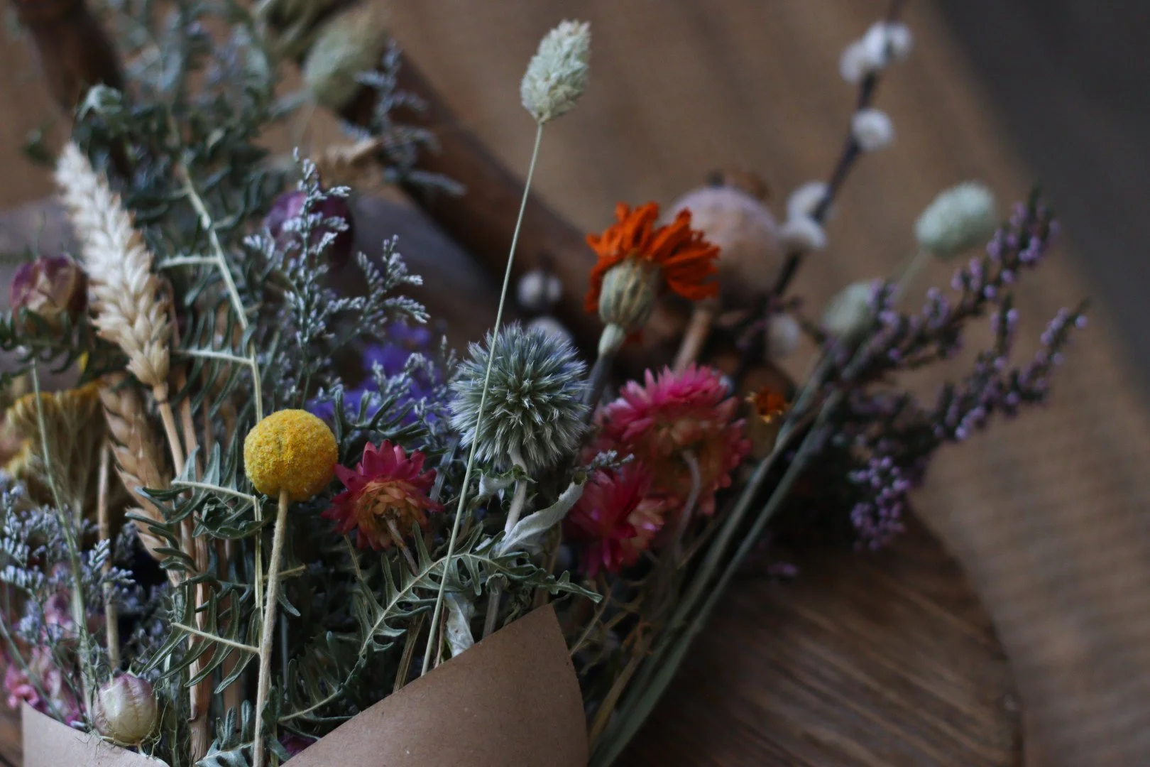 Close-up of a bouquet of dried flowers wrapping in brown paper, placed on a wooden surface.