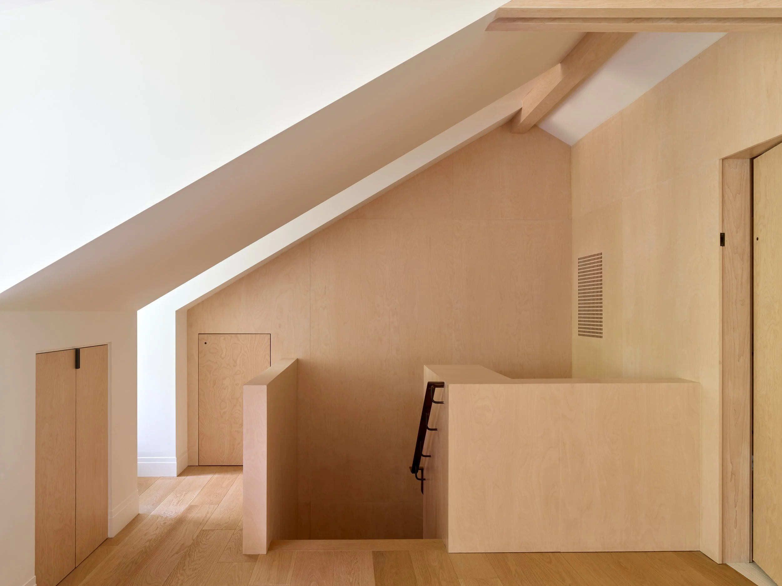 Interior view of a modern room with light wood walls, a folding door, a staircase with black railings, and a sloped ceiling.