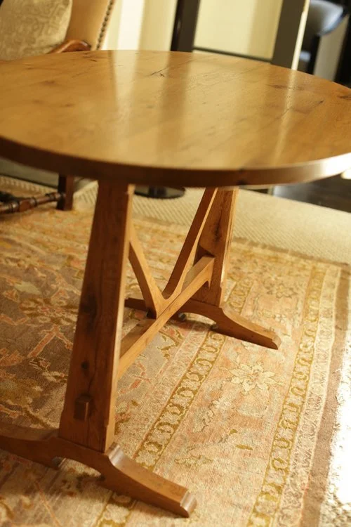 A round wooden table with a pedestal base standing on a patterned area rug in a living room.