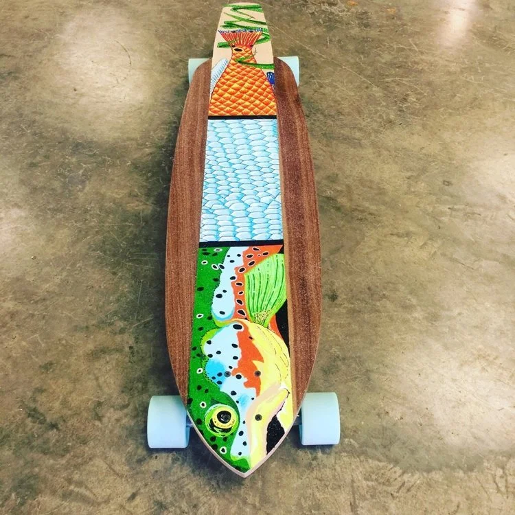 A longboard skateboard with colorful marine-themed artwork on the deck, featuring a fish and water design, with light blue wheels and a natural wood finish.