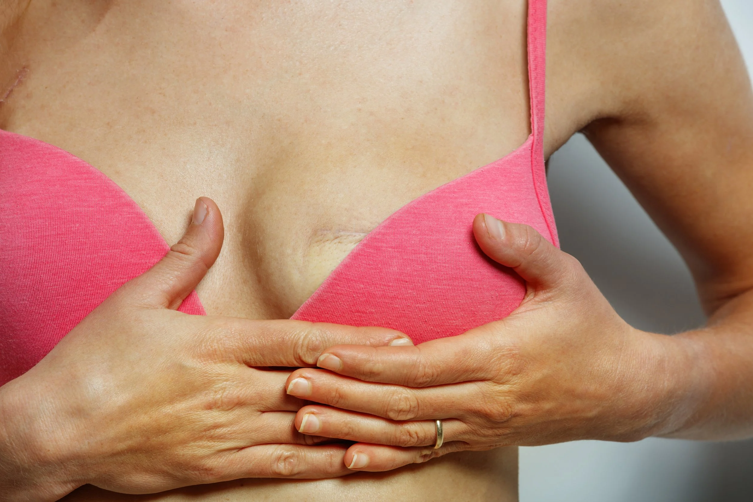 A woman in a pink tank top holding her breast with both hands.
