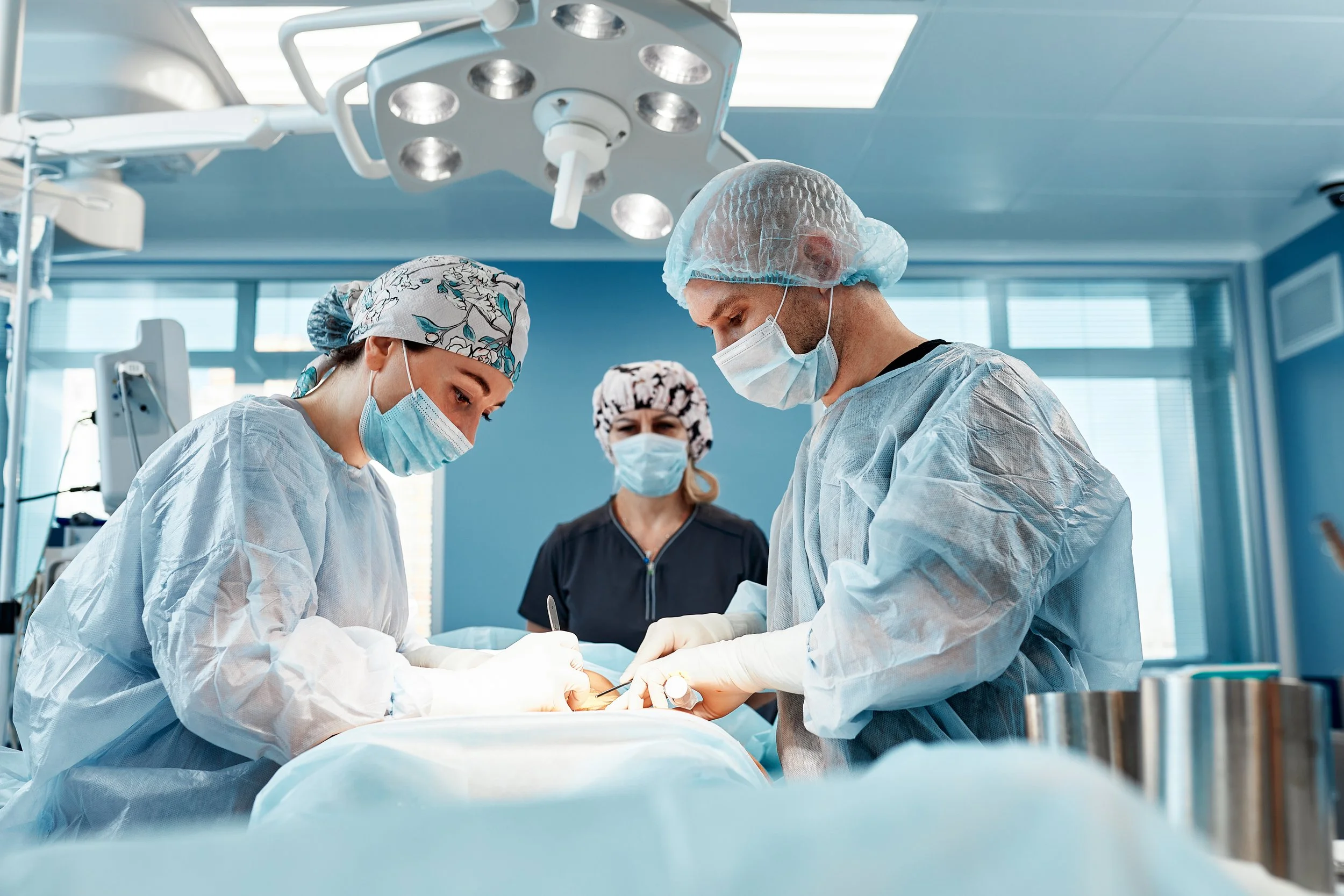 Medical team performing surgery in an operating room with surgical lights overhead.