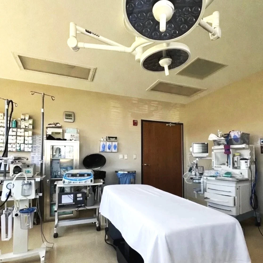 Hospital operating room with medical equipment, an operating table covered with a white sheet, and surgical lights overhead.