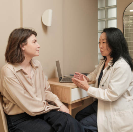 Medical consultation between a female doctor and a young woman in an office setting.