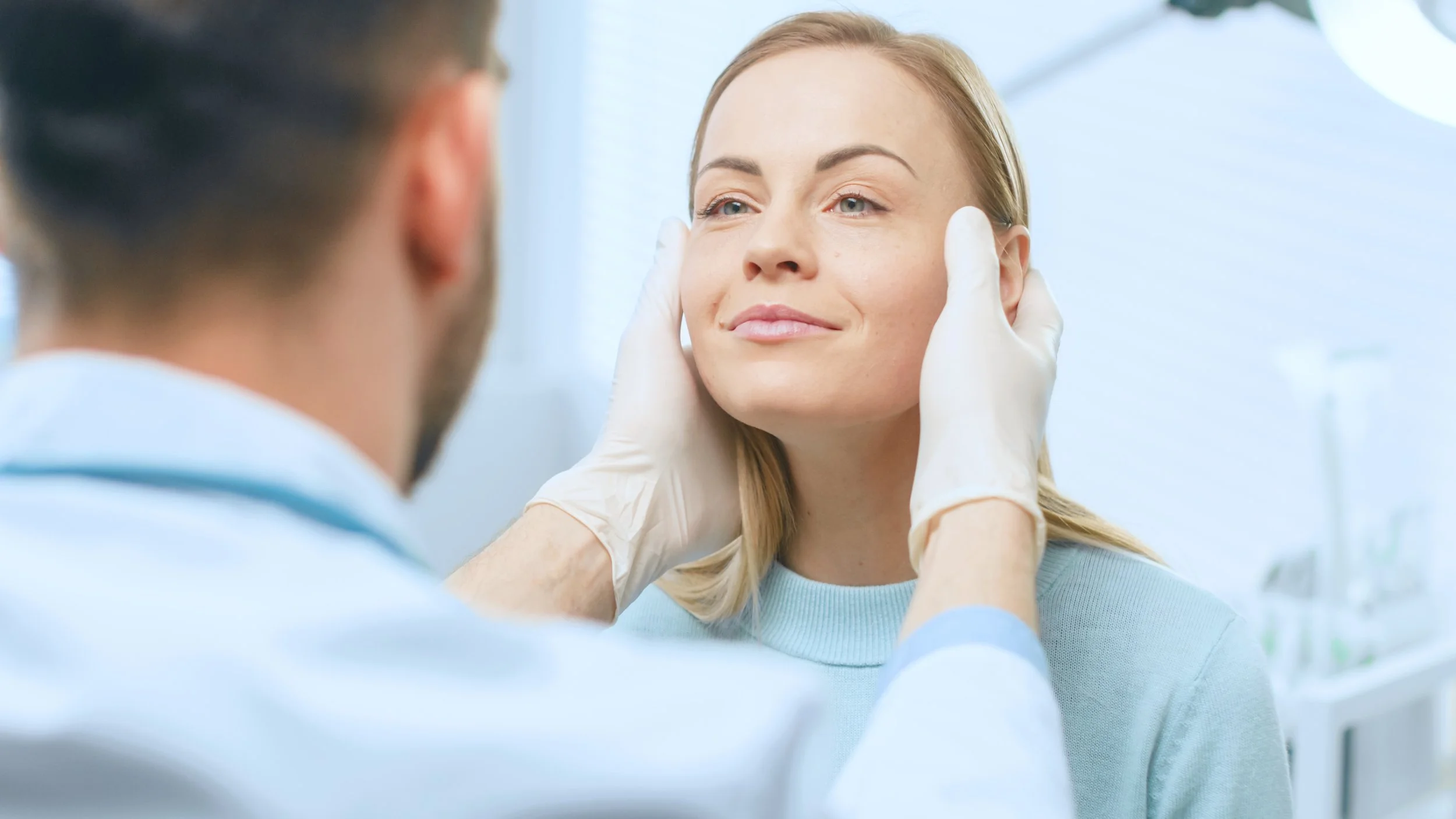 A female patient smiling during a medical consultation, with a healthcare professional gently holding her face.
