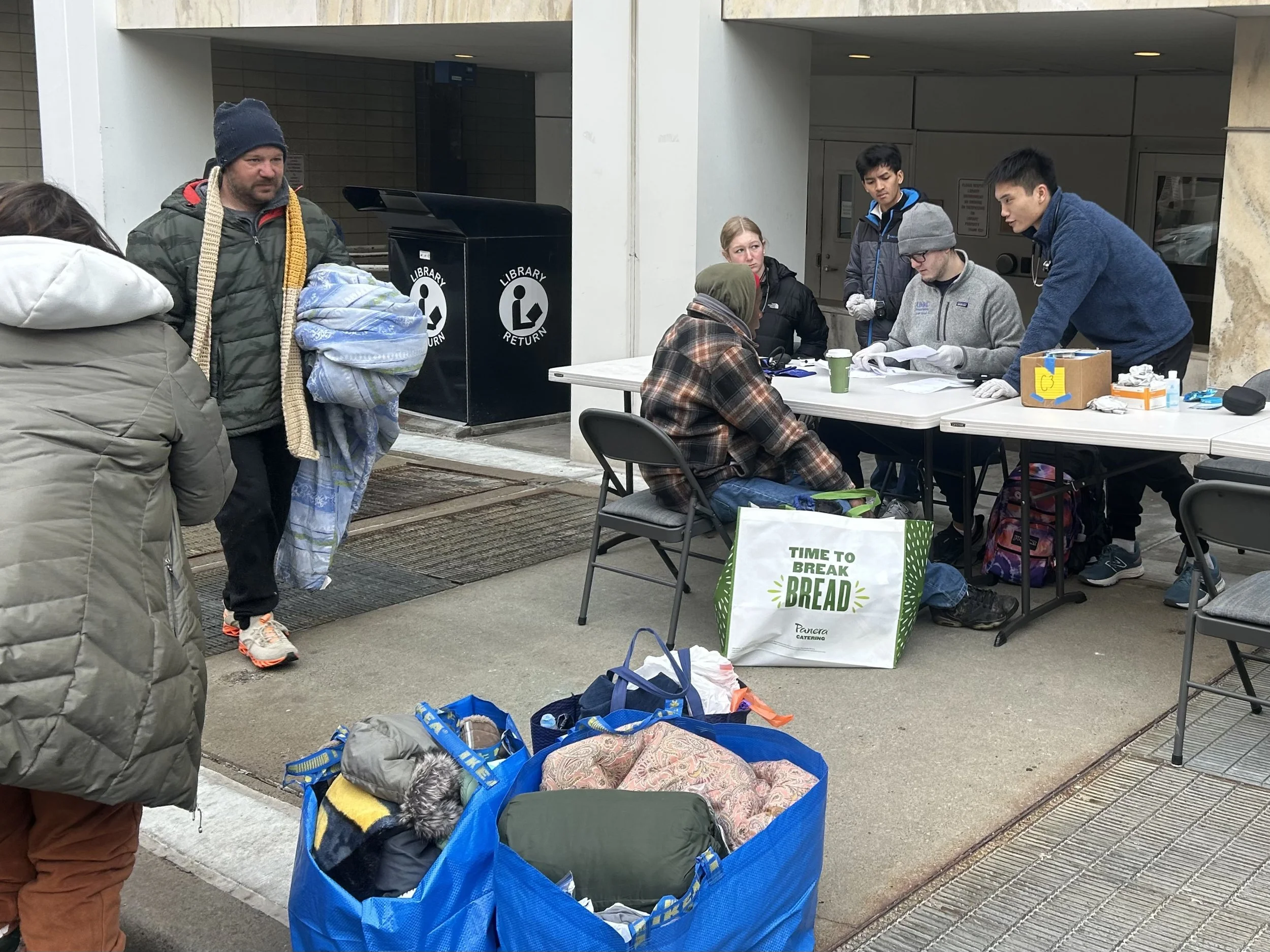 People standing and sitting at outdoors table at a Street Support KC event.