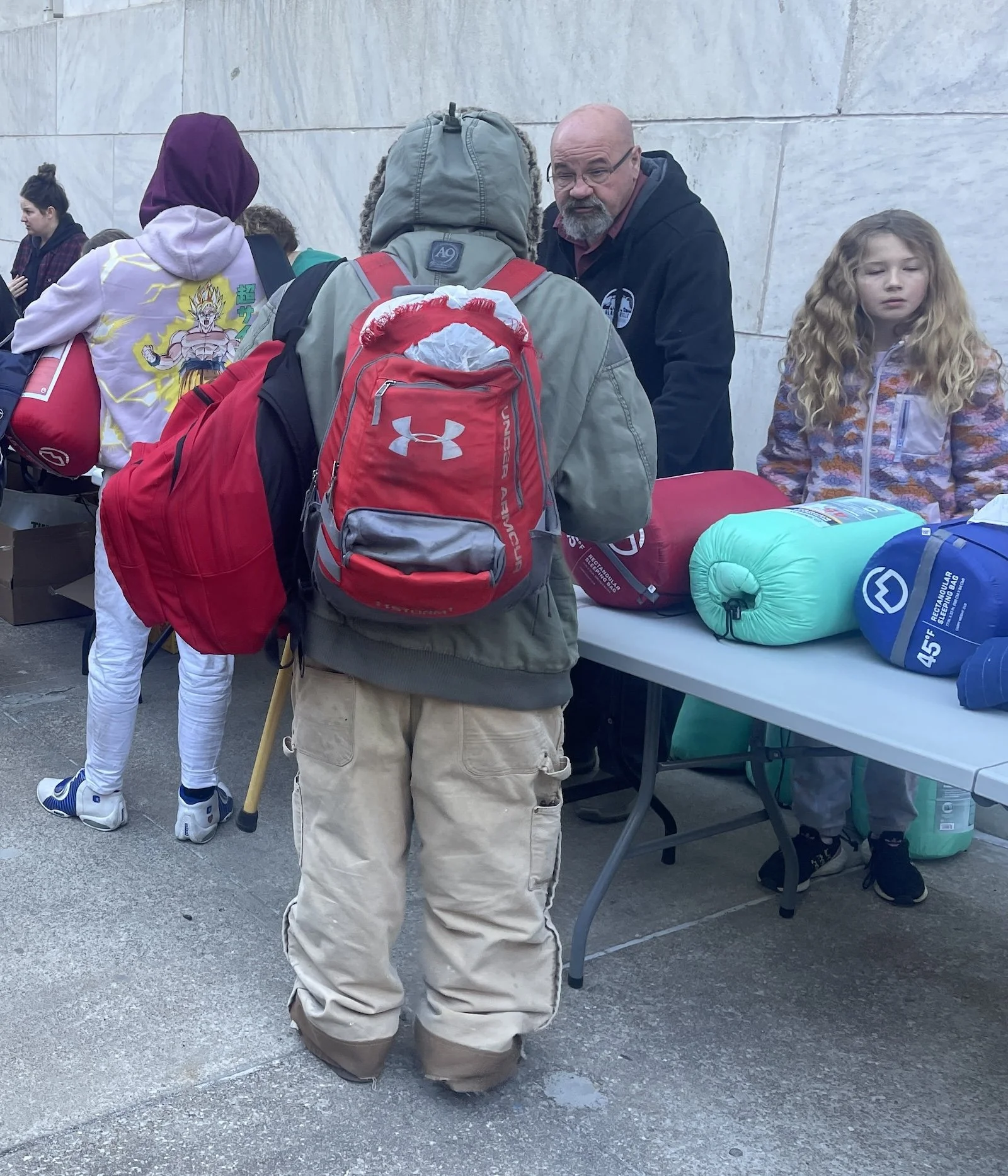 People gathered around a table at Street Support KC event with camping gear, sleeping bags, backpacks, and pillows.
