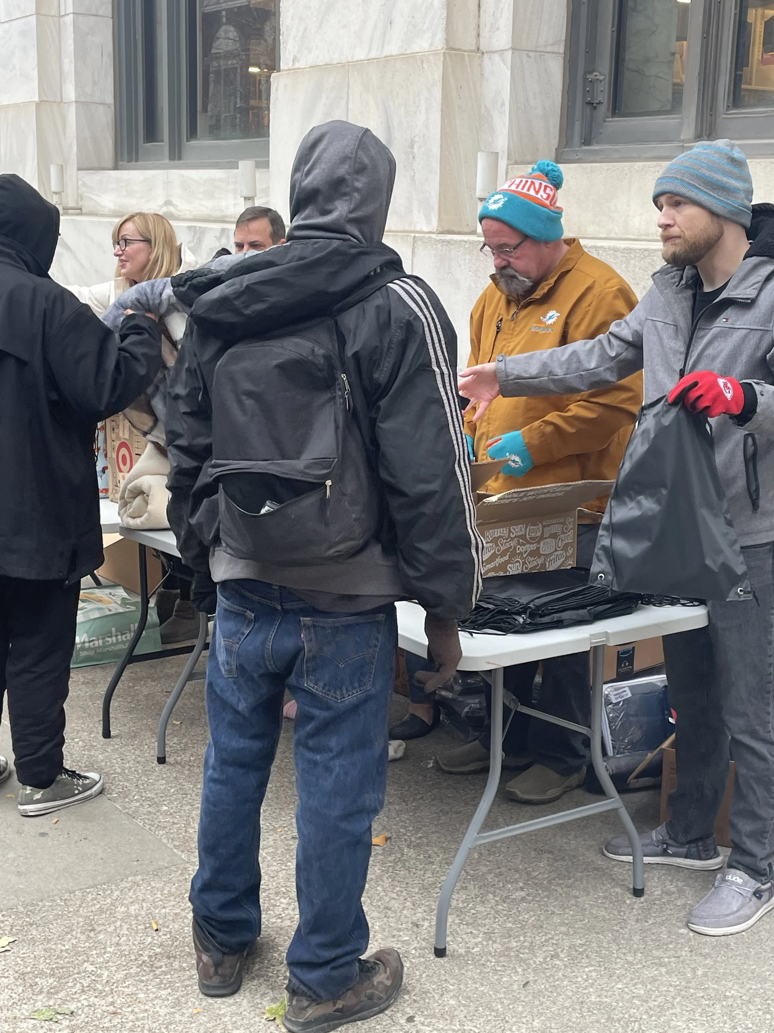 People standing at a Street Support KC table outdoors, receiving food and supplies from volunteers.