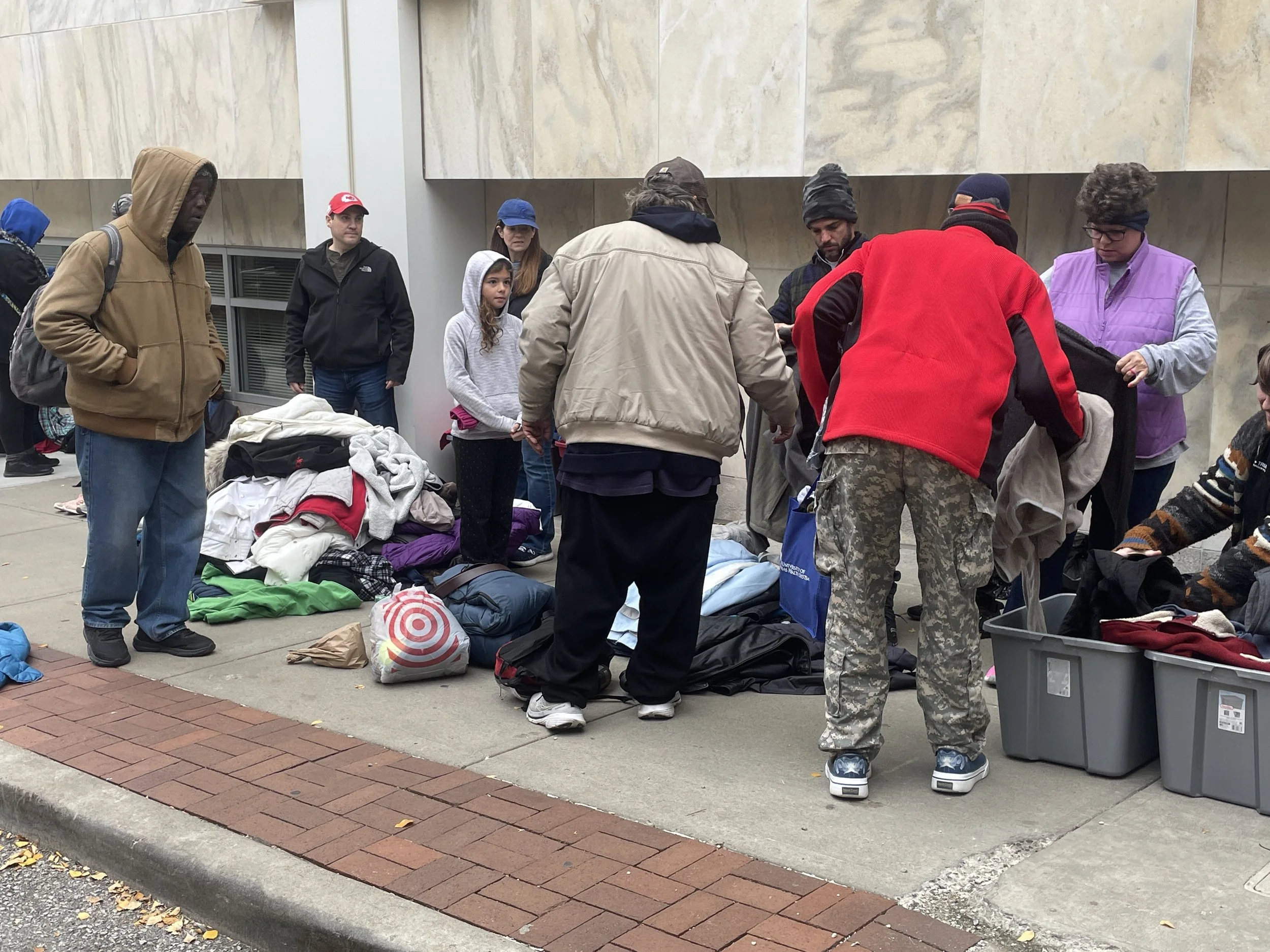 A group of people gathered around piles of clothing at a Street Support KC event.