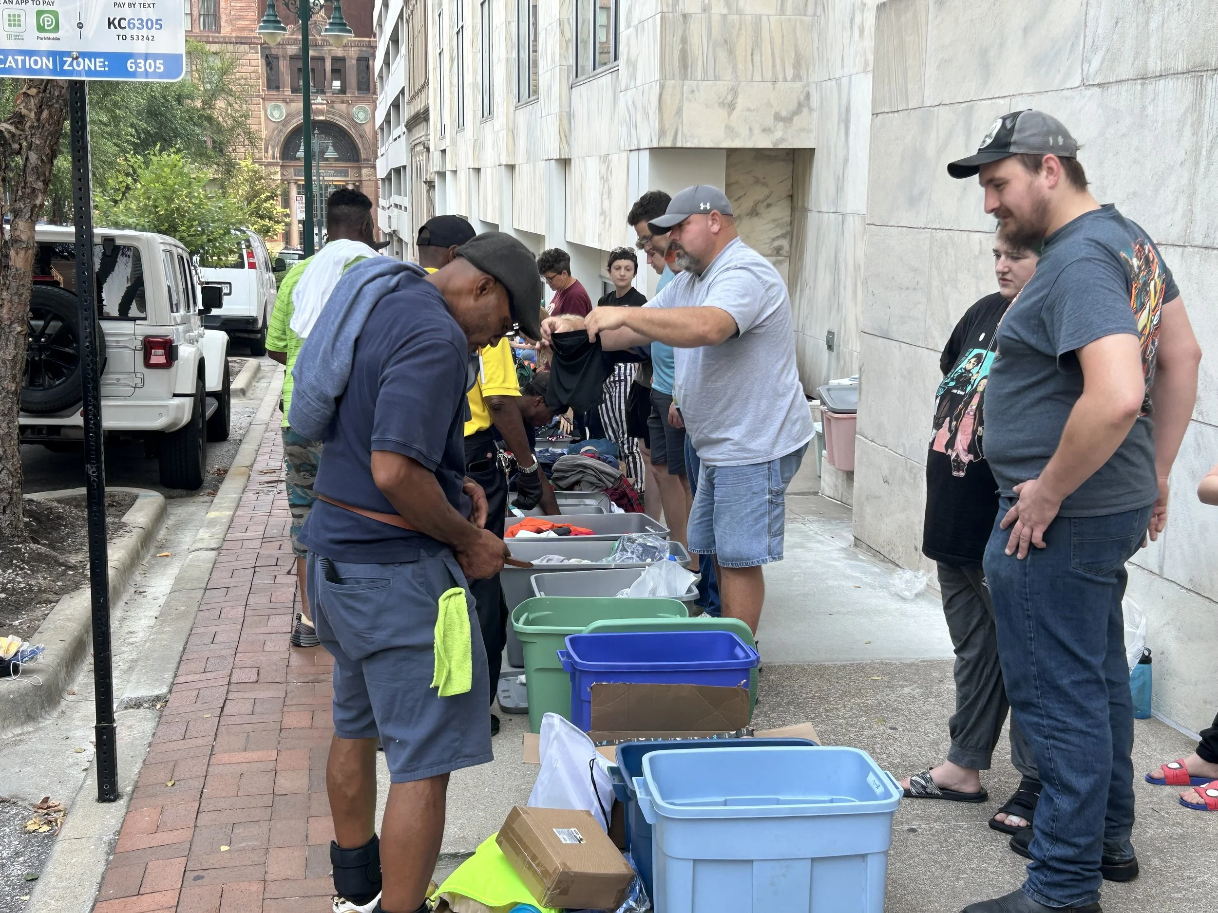 Homeless men and women standing in line on a sidewalk, receiving items from Street Support KC.