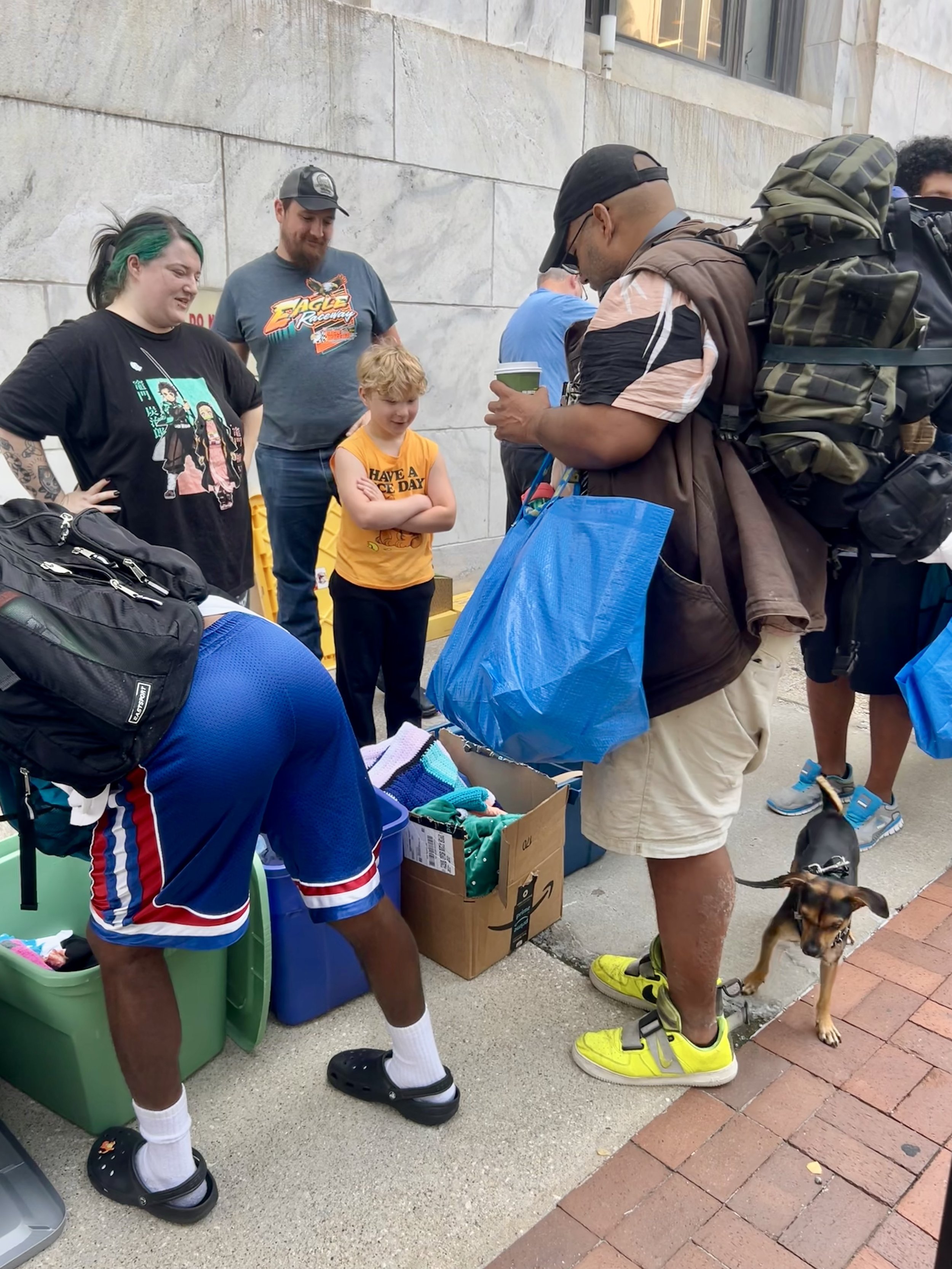 Group of people gathered at Street Support KC around a table of donated clothes and items outside the downtown Library.