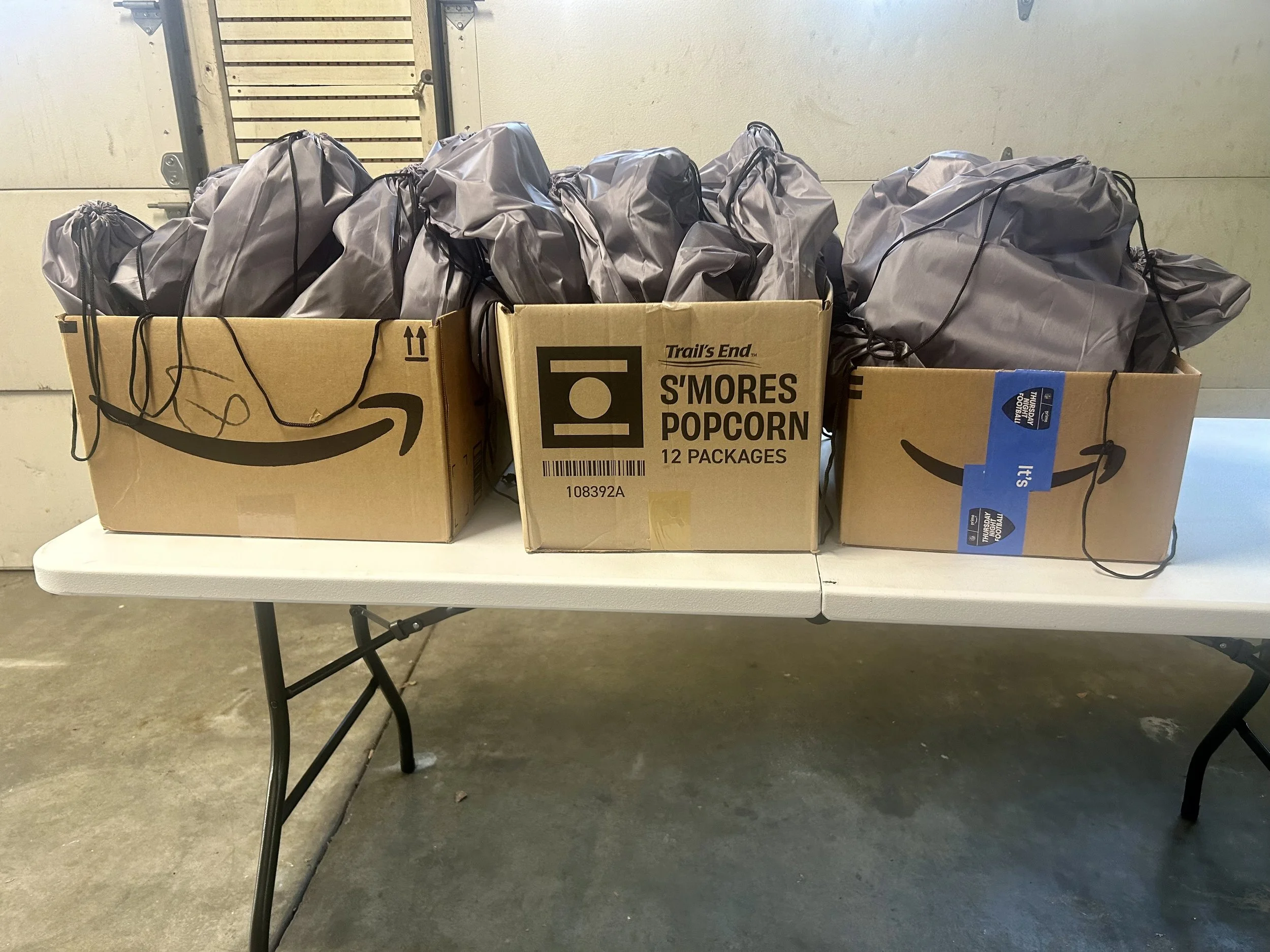 Three cardboard boxes filled with gray drawstring bags on a white folding table.