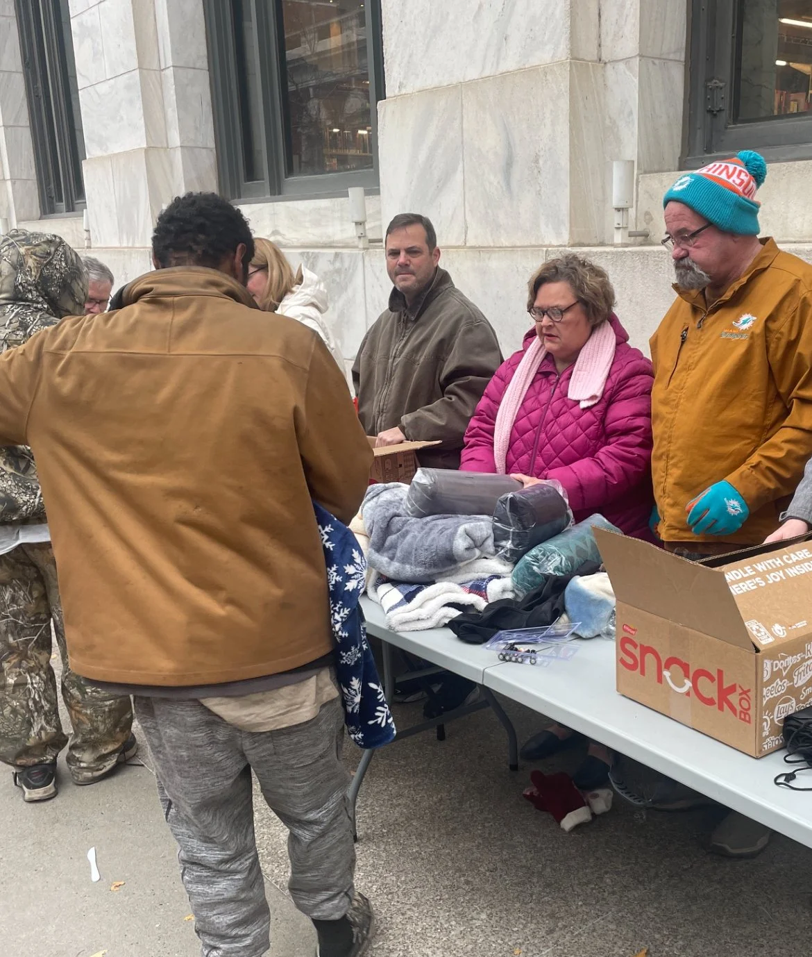 Homeless people are at a Street Support KC table distributing and receiving clothing and supplies during a cold weather event.