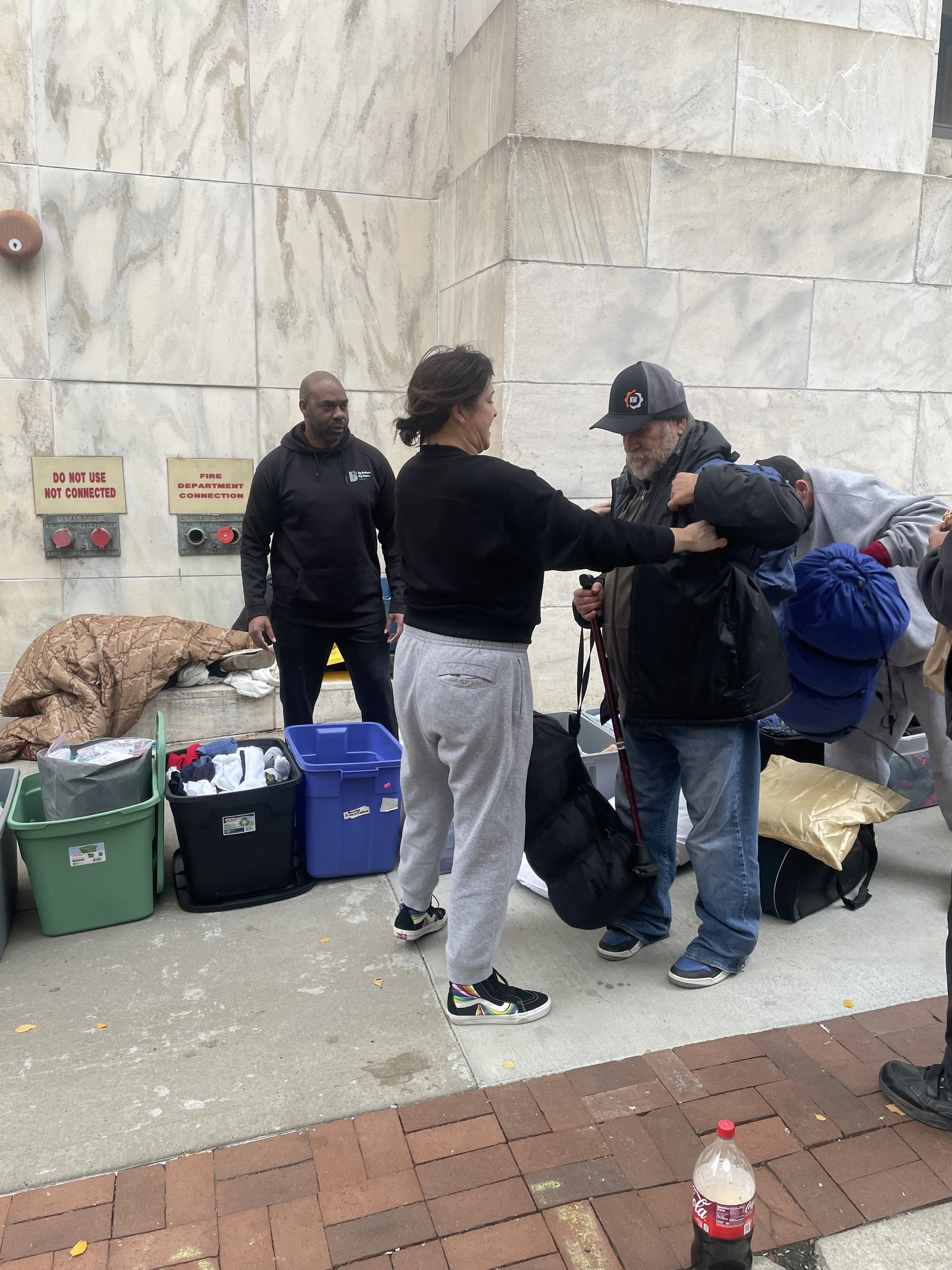 Homeless people are standing outside receiving essential items at a Street Support KC event in Kansas City, Missouri.