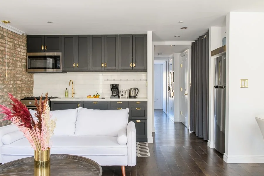 Open-plan living room and kitchen with black cabinets, white walls, and dark hardwood floors.