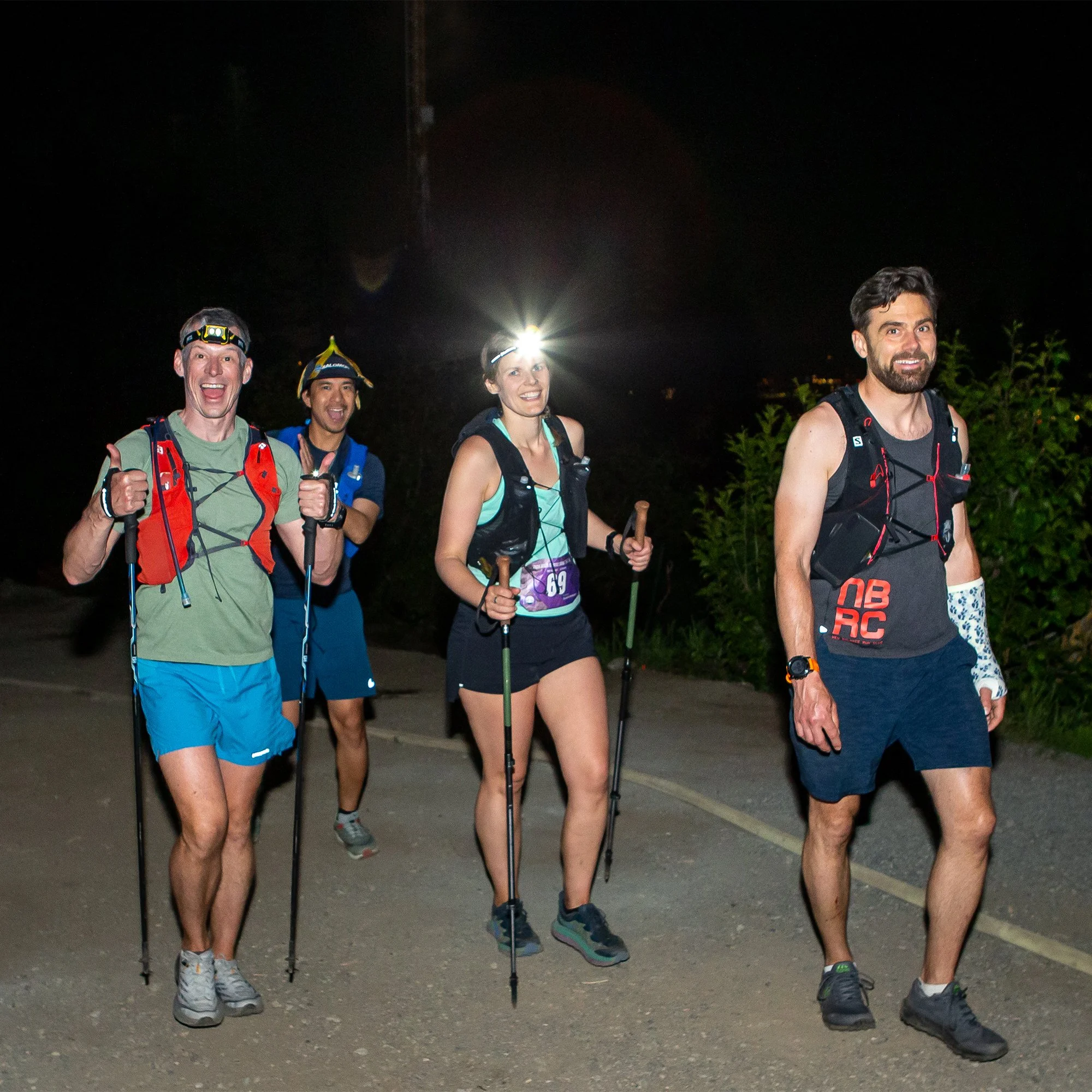 Four friends trail running at night, wearing headlamps and athletic gear, smiling and enjoying a nighttime outdoor run.