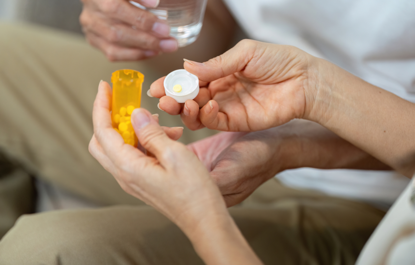 Person opening a bottle of pills while another person holds a glass of water.