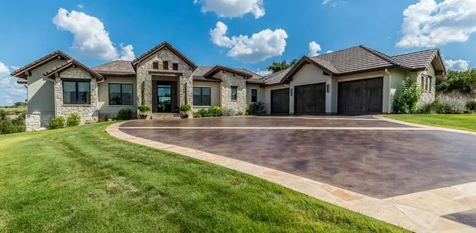 brand new beautiful residential concrete driveway with green landscaping and stone house
