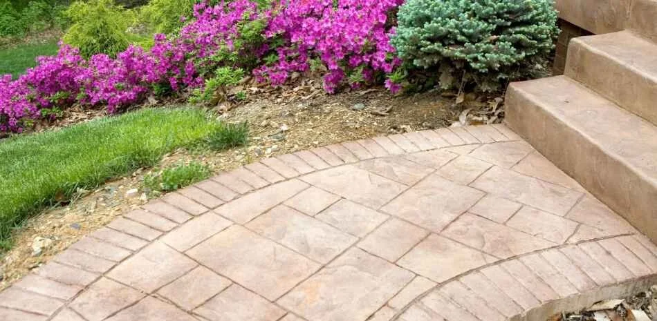 stamped concrete walkway with pink flowers and green landscaping