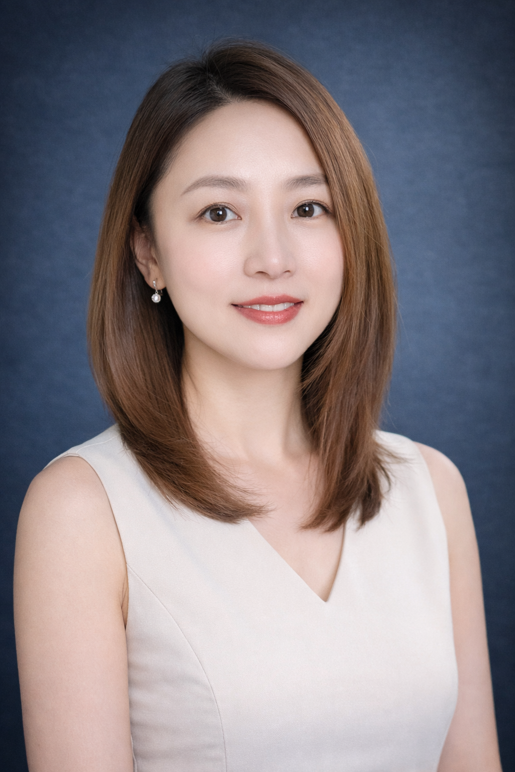 Headshot of a woman with shoulder-length brown hair, wearing a sleeveless light-colored top and pearl earrings, against a dark blue background.