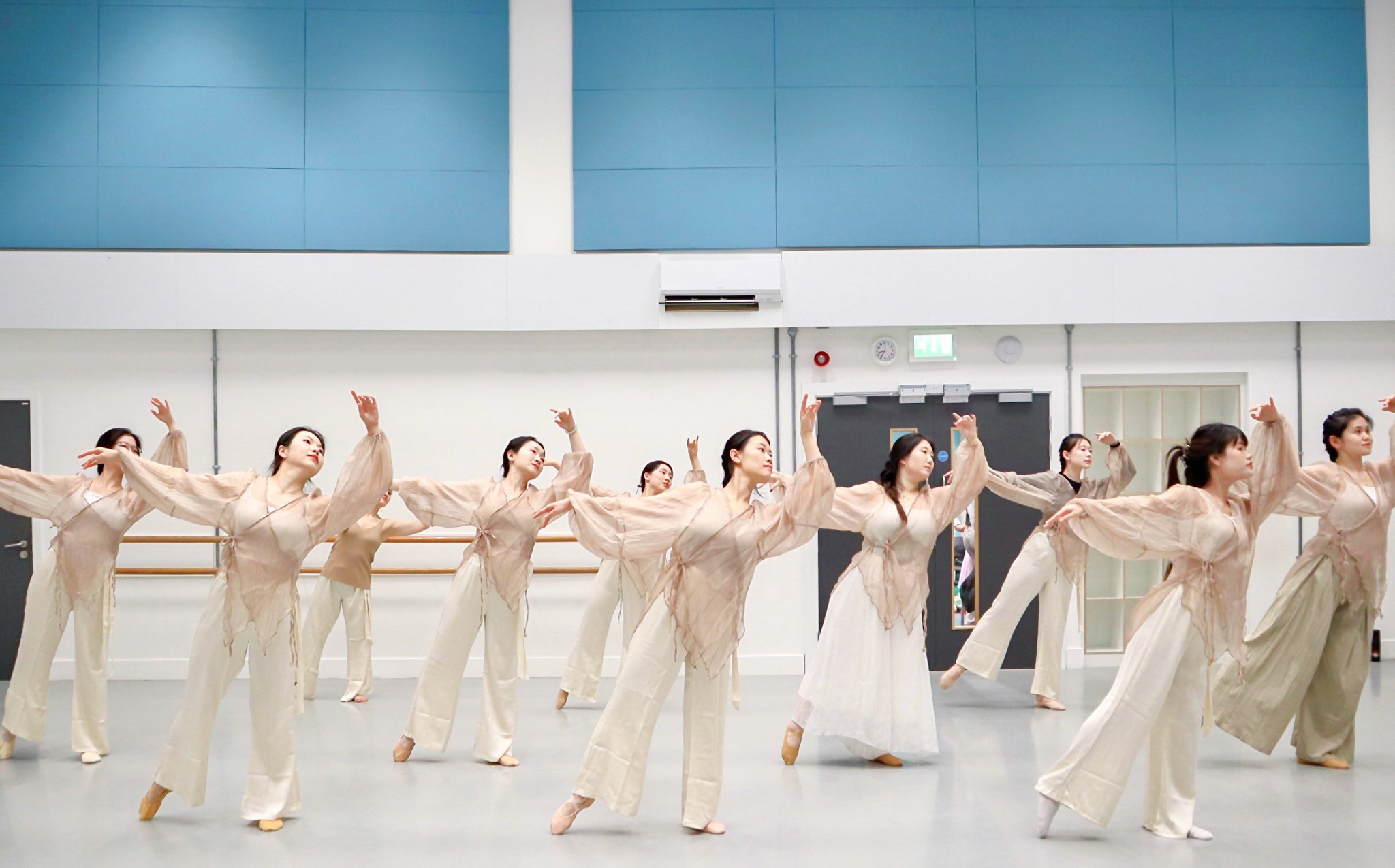 Group of women in beige costumes performing ballet in a dance studio.