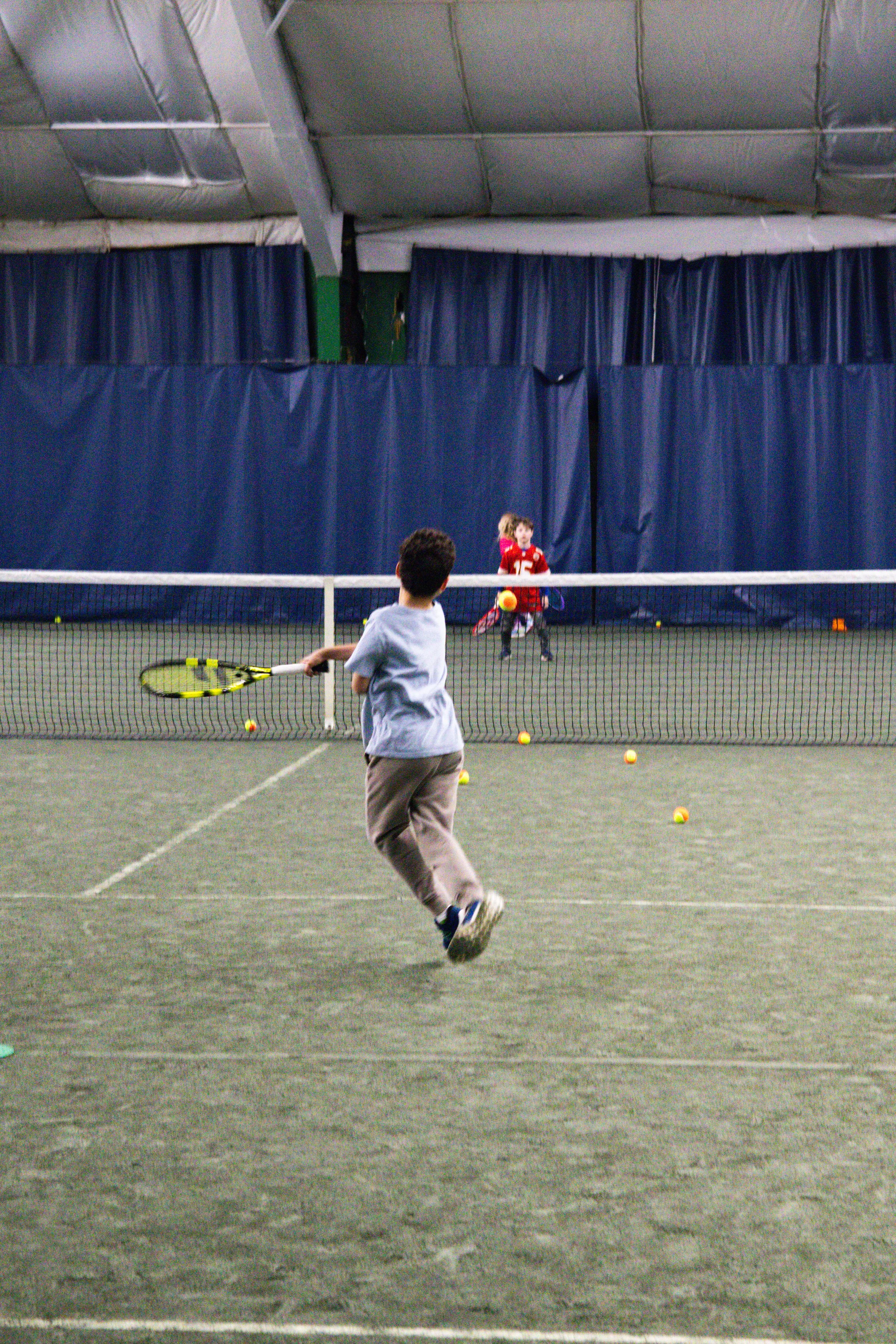 Child practicing tennis indoors at Westport Tennis Club with scattered training balls on the court.