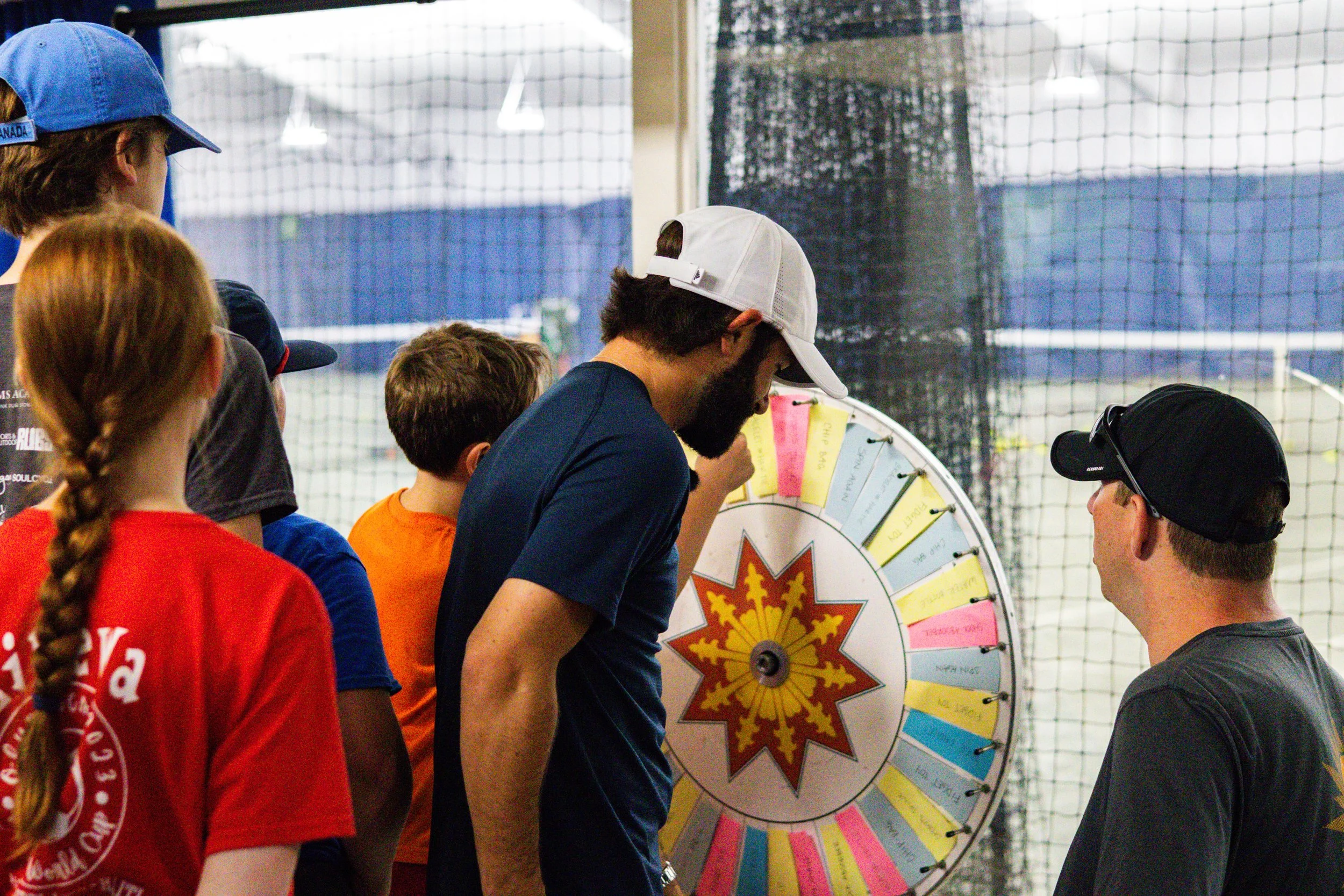 Children and coach gathered around a prize wheel during Westport Tennis Club’s junior summer camp event.