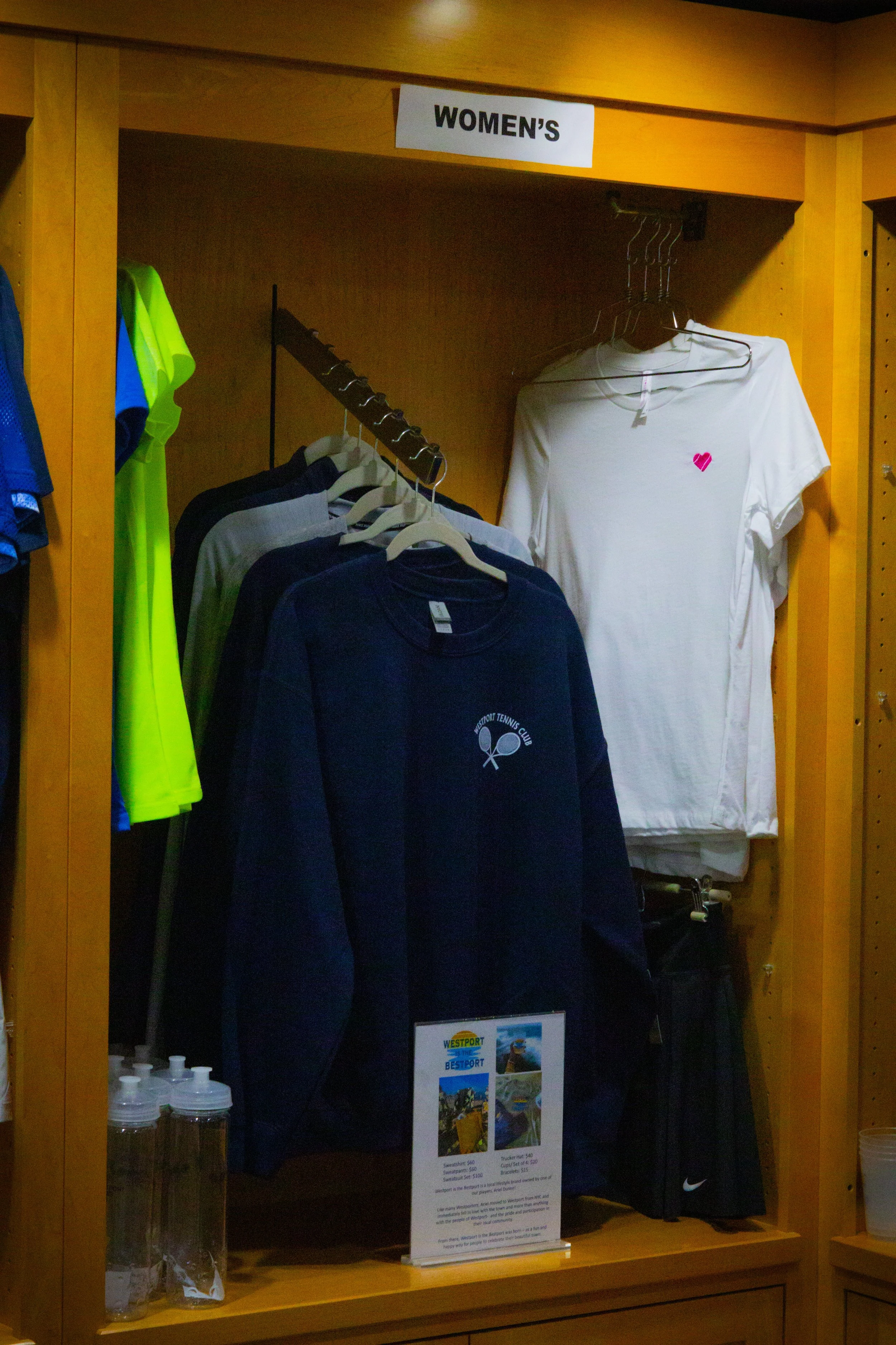 Women’s tennis clothing section at Westport Tennis Club, featuring sweatshirts, T-shirts, water bottles, and accessories.