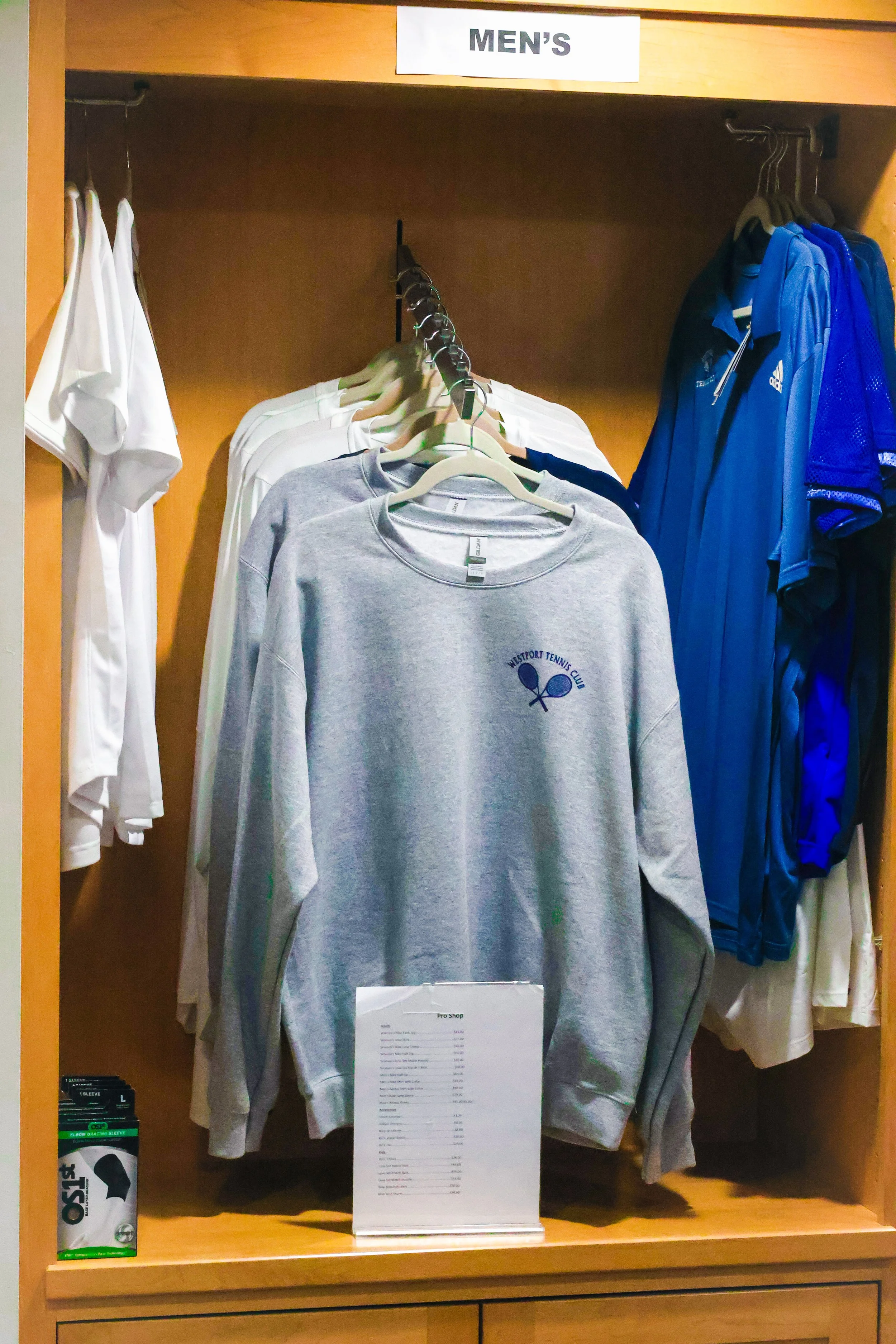 Men’s Westport Tennis Club apparel display featuring logo sweatshirt, athletic socks, and performance jackets inside the pro shop.