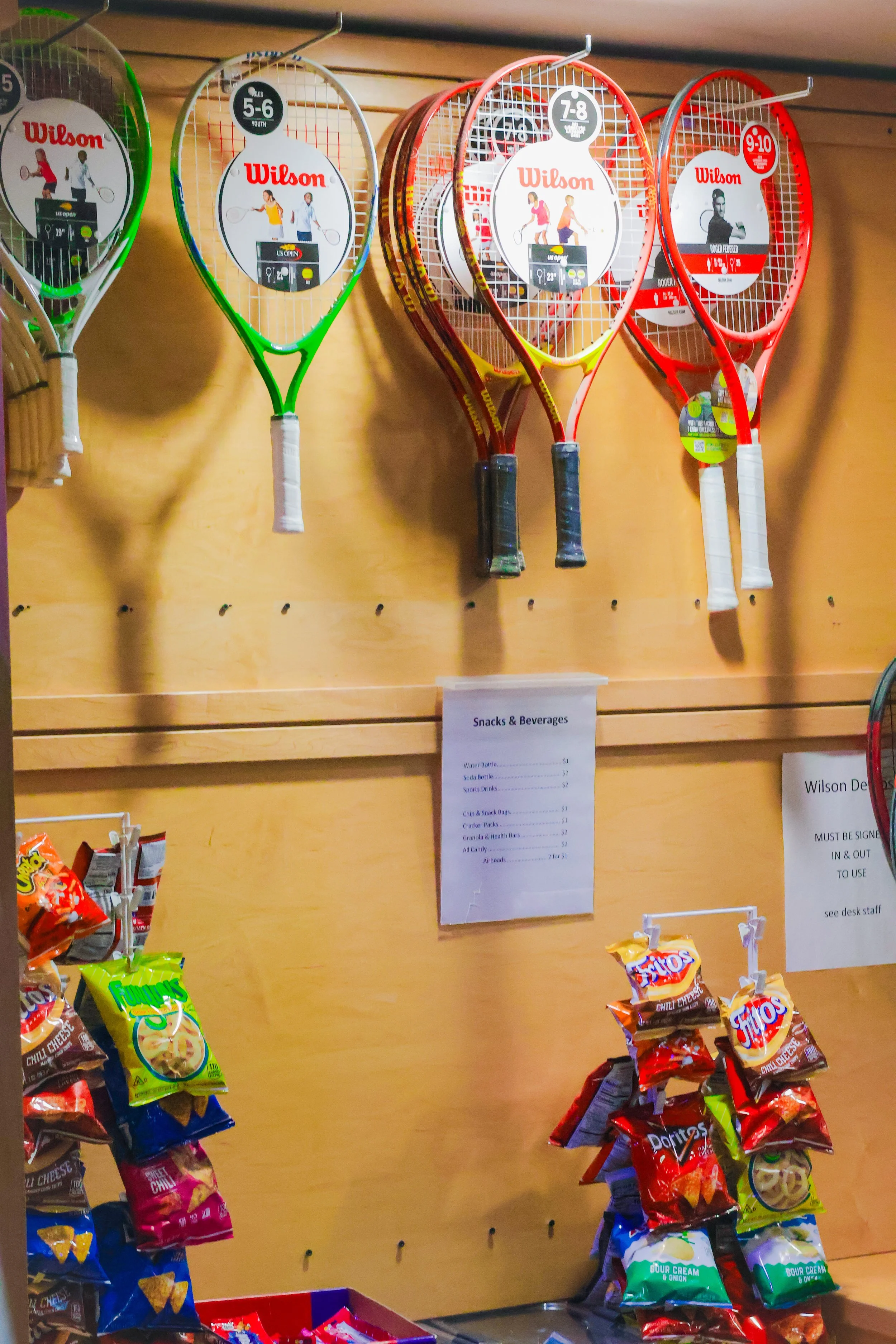 Wilson junior tennis racquets in multiple sizes (ages 5–10) displayed on wall inside Westport Tennis Club pro shop.