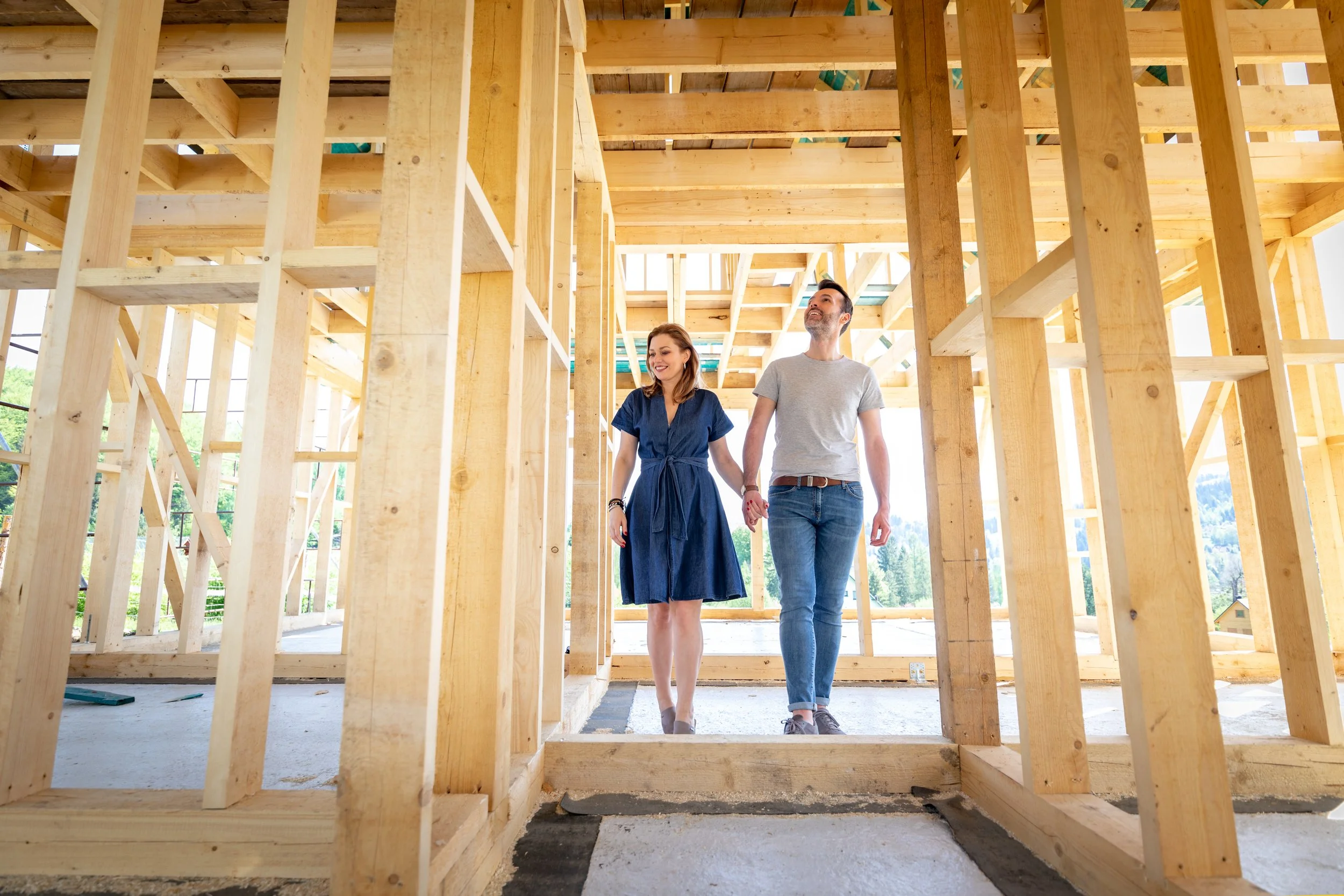 A couple walking inside a house under construction, with exposed wooden framework.