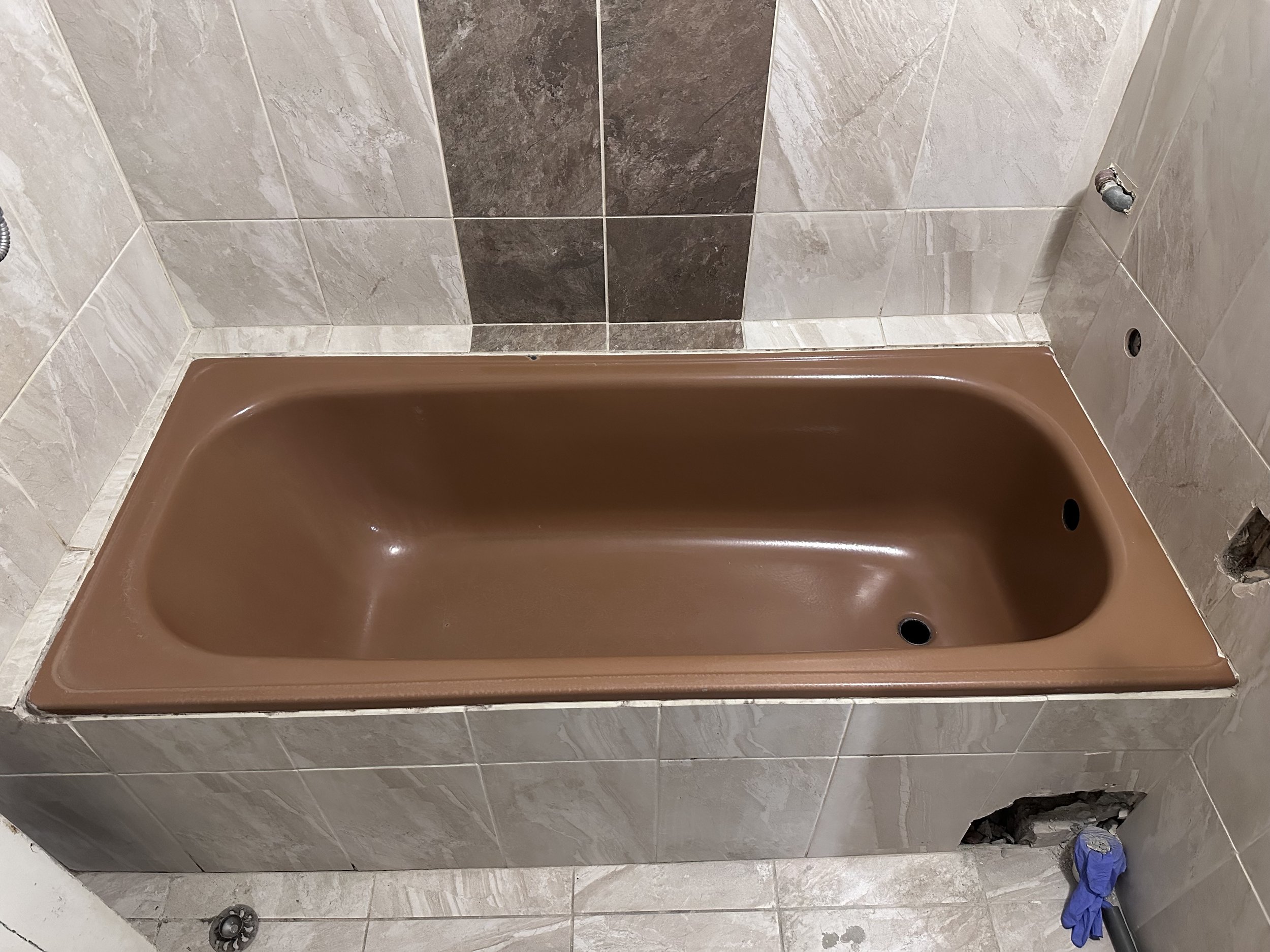 Brown bathtub installed in a tiled bathroom, surrounded by beige and brown tiles, with plumbing fixtures not yet attached.