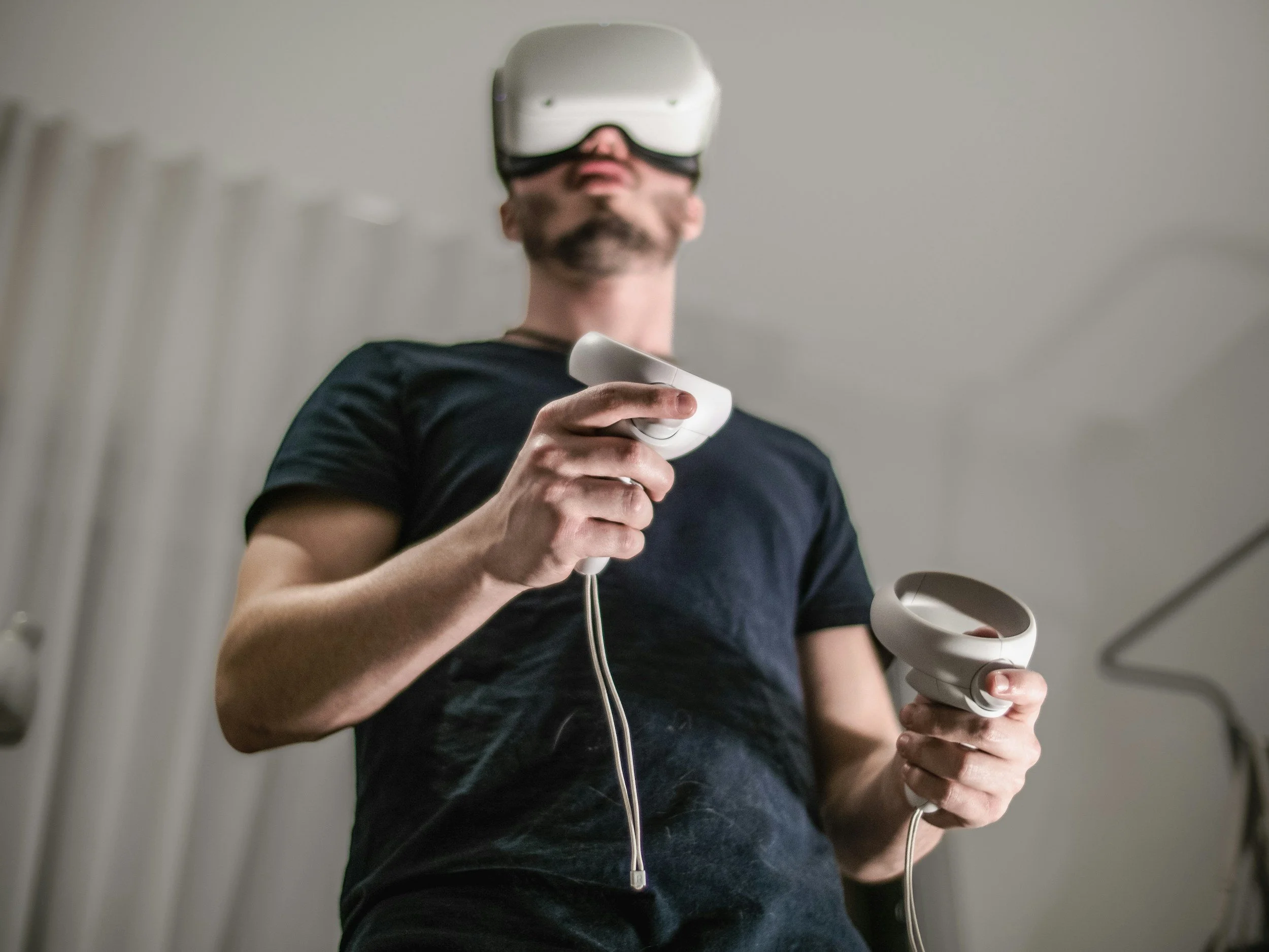 Man wearing virtual reality headset holding controllers in a room with white curtains.