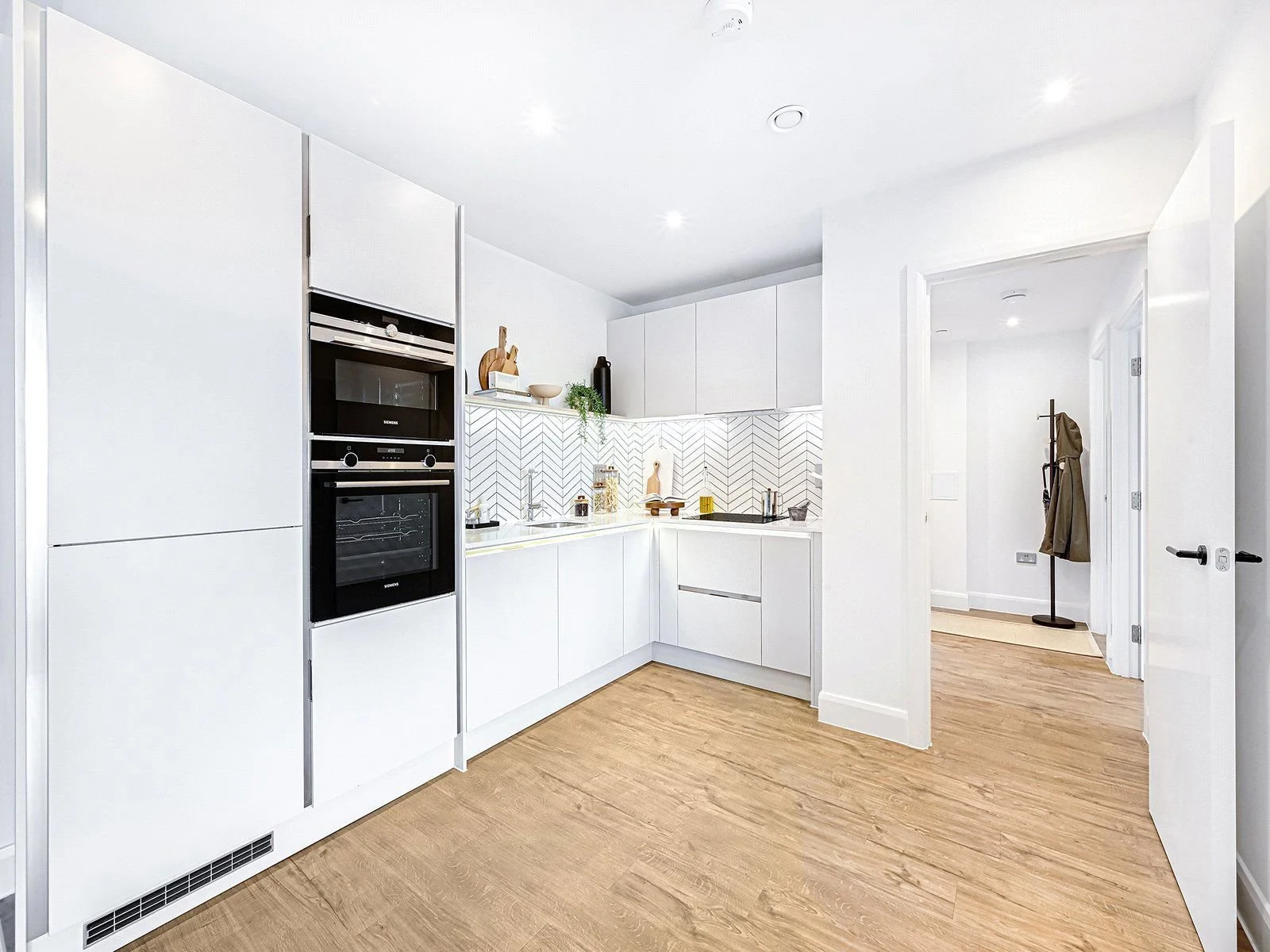 Modern white kitchen with built-in black appliances, white cabinets, a white countertop, and wooden flooring.