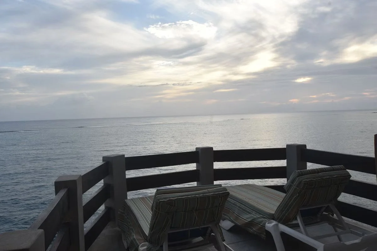 Two Patio lounge chairs on Terrace of Shipwatchers Studio,  overlooking a calm ocean and cloudy sky at sunset.