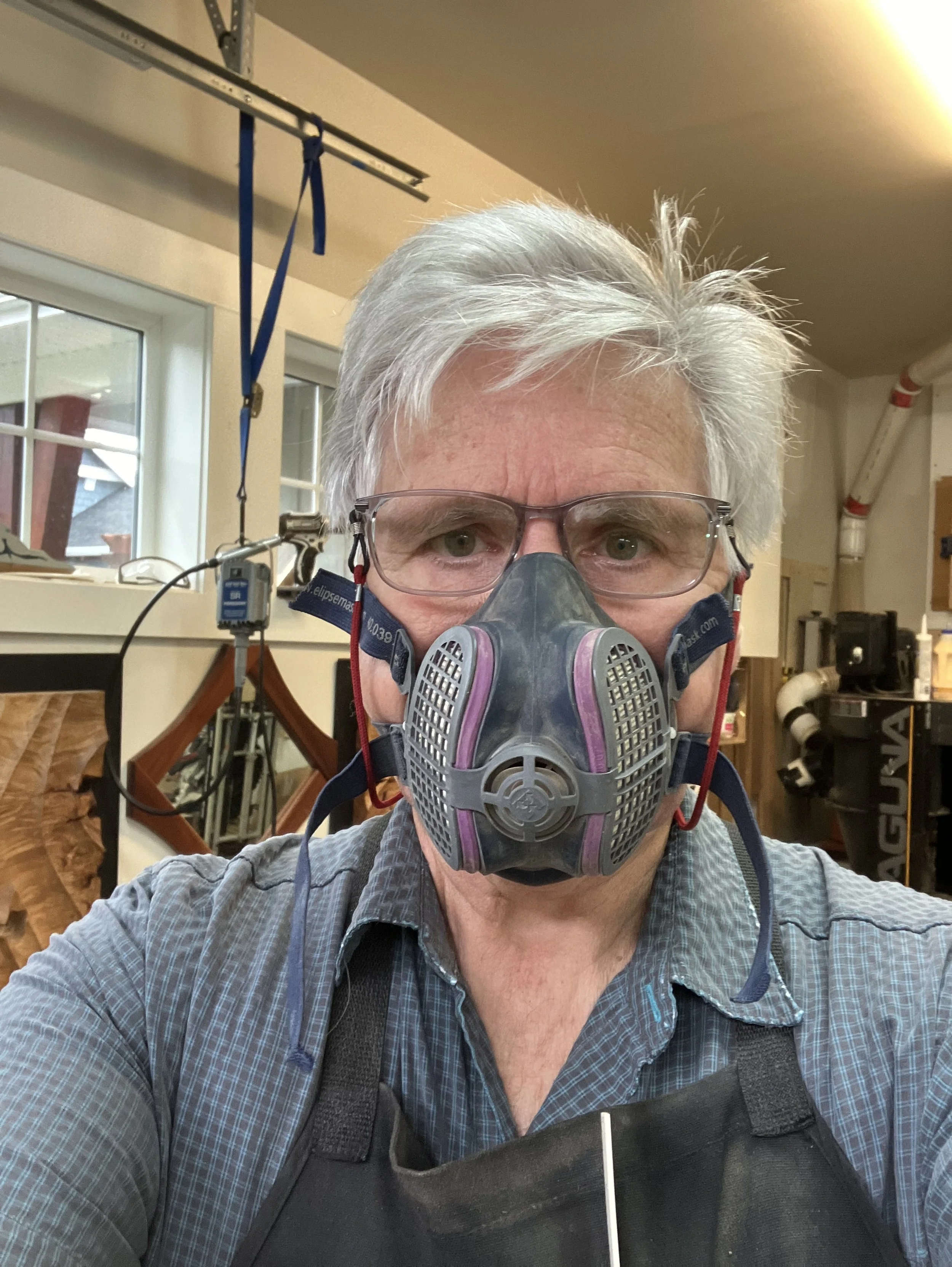 Man with gray hair wearing glasses and a respirator mask in a workshop