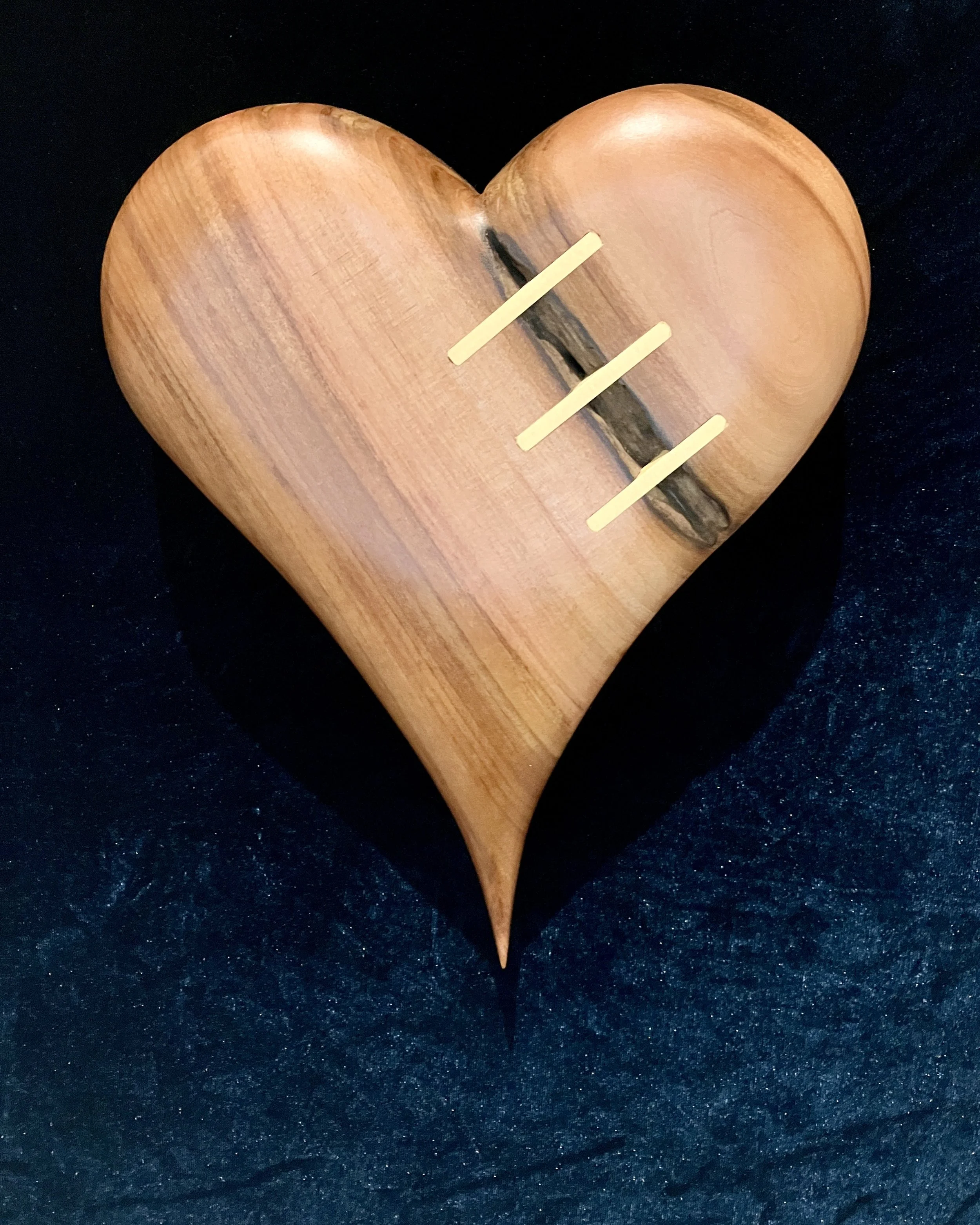 A wooden heart-shaped object with three horizontal yellow sticks and a dark streak running through its middle, set against a black background.
