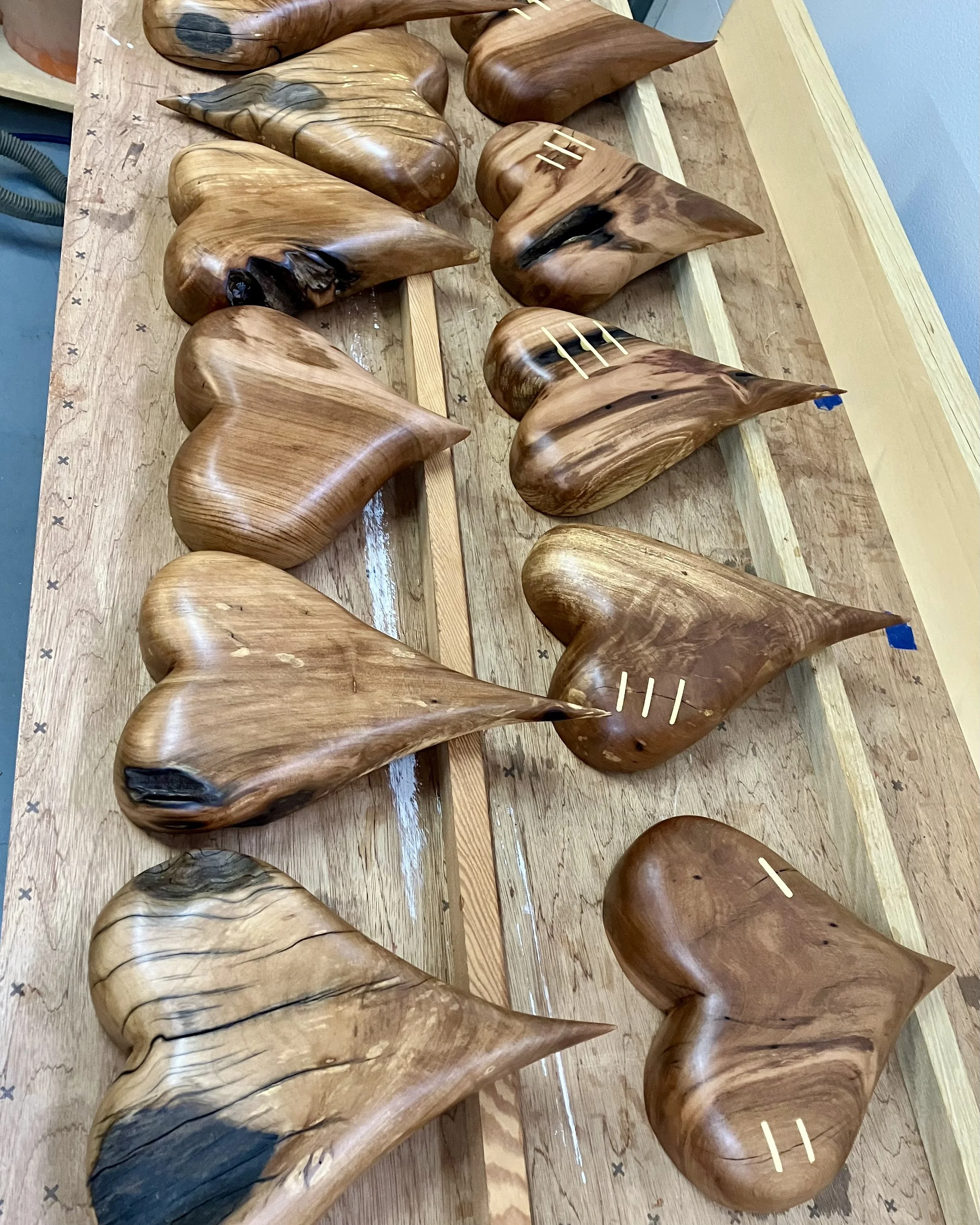 A collection of wooden sculptures with smooth, abstract, heart-shaped and pointed designs on a wooden workbench.