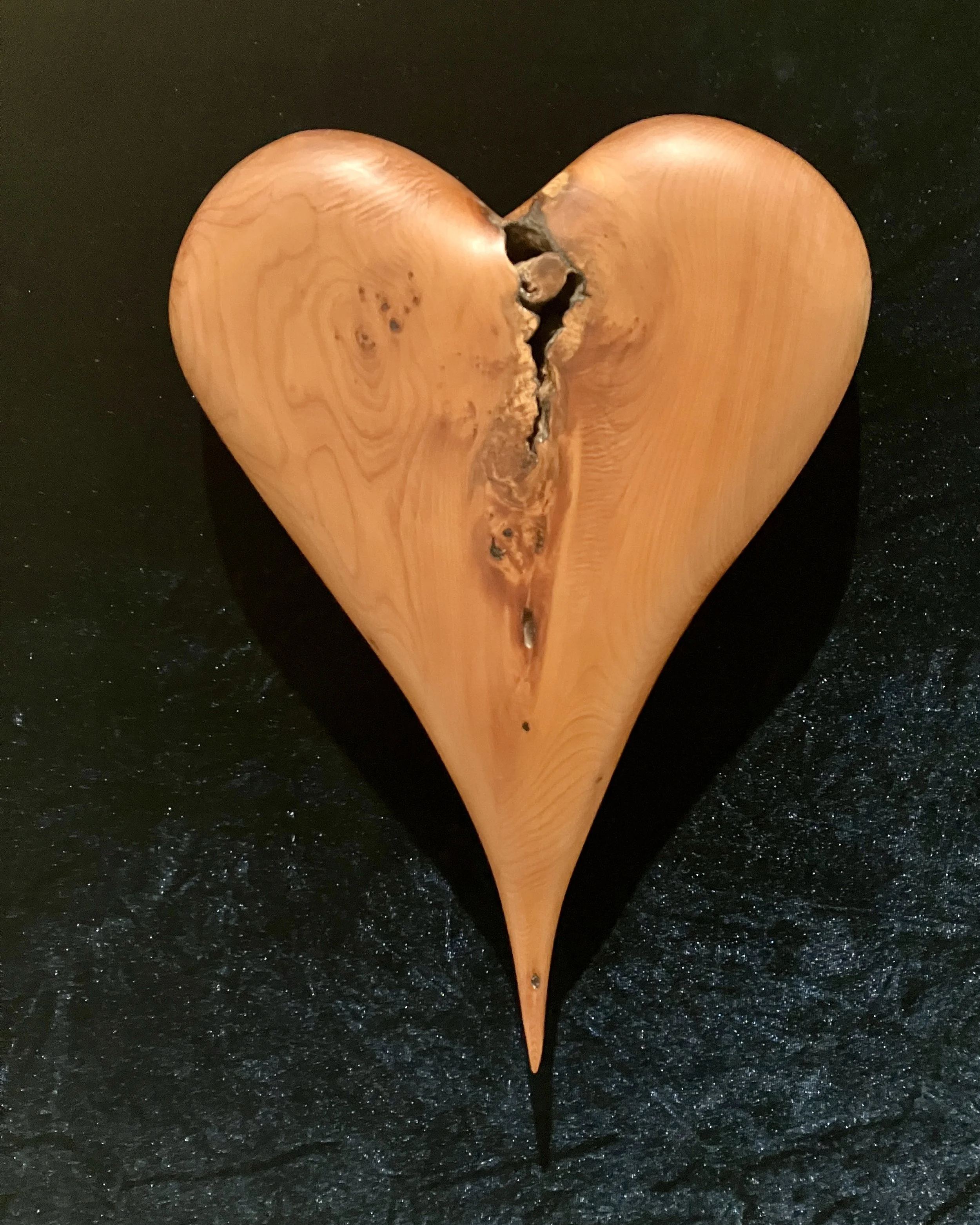 Wooden heart sculpture with a natural, polished finish and visible wood grain, placed on a black surface.