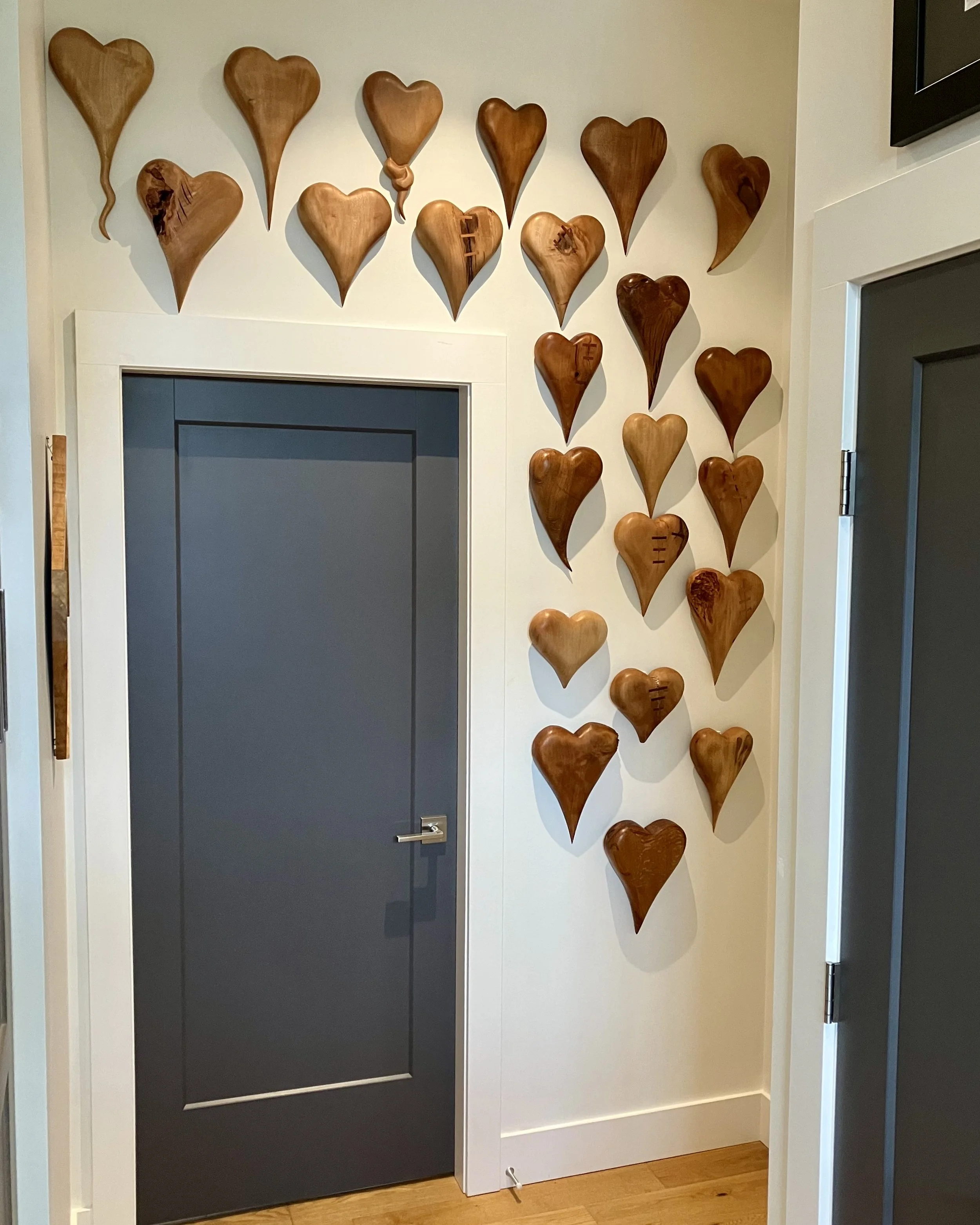 Wall decorated with multiple wooden heart-shaped art pieces arranged around a doorway.