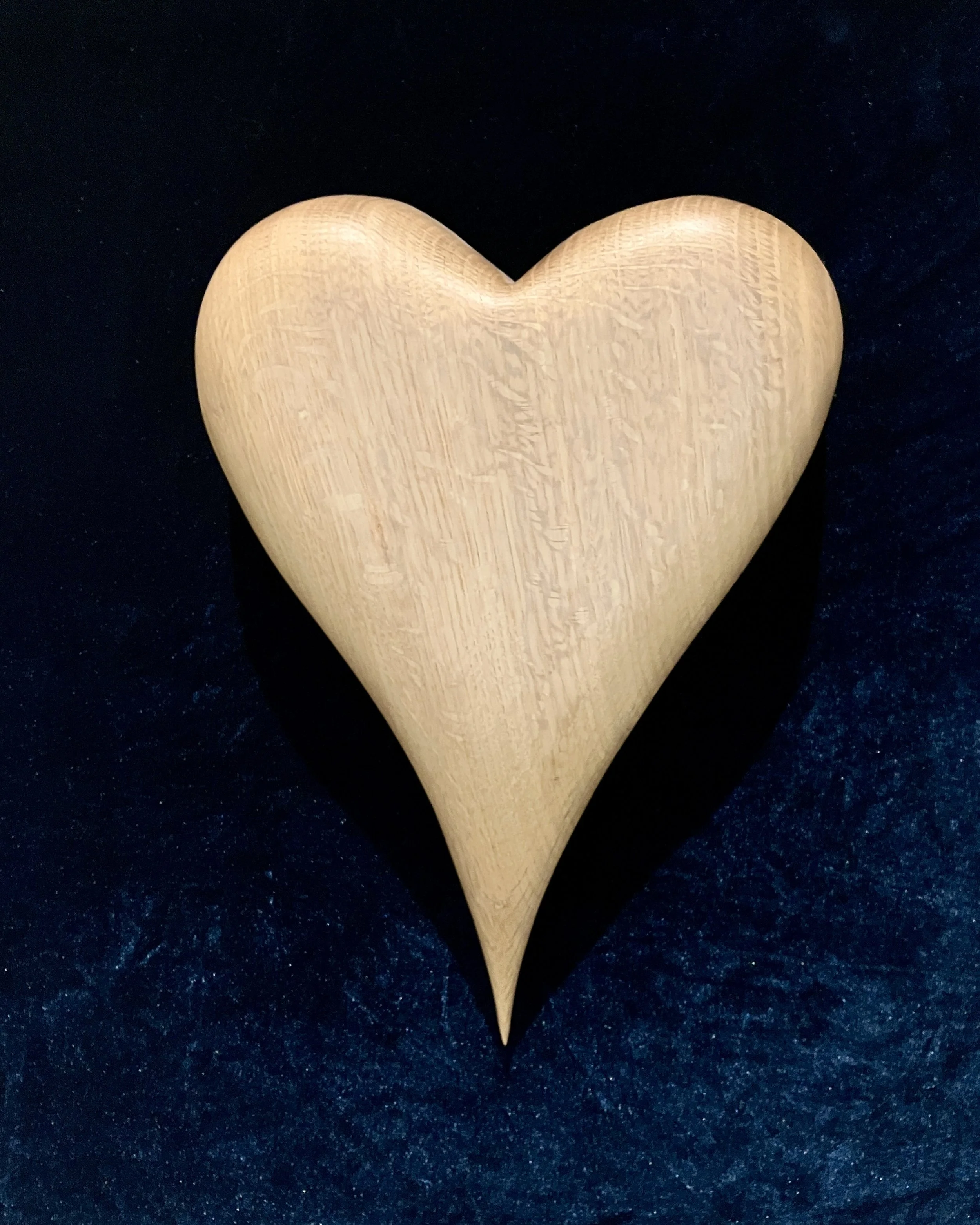 A smooth, wooden heart sculpture on a dark, textured background.